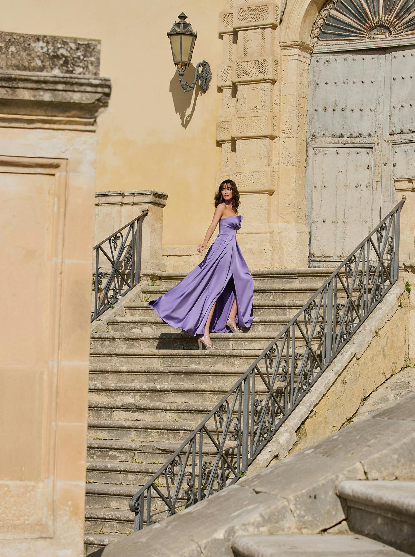A woman wearing a purple dress walks down a staircase, embodying grace and style in her descent.