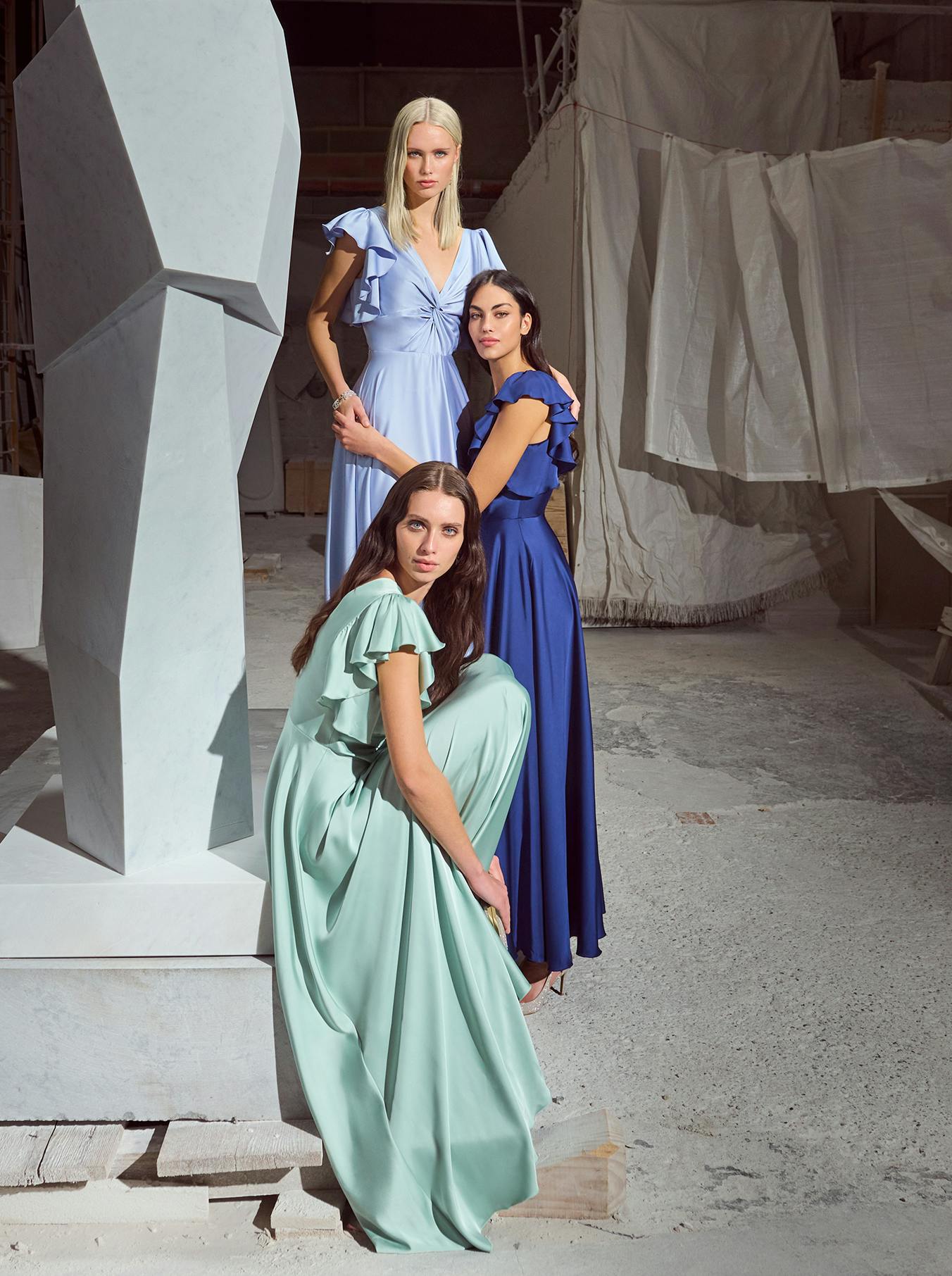 Three women smiling and posing together in front of a large, abstract sculpture in an outdoor setting