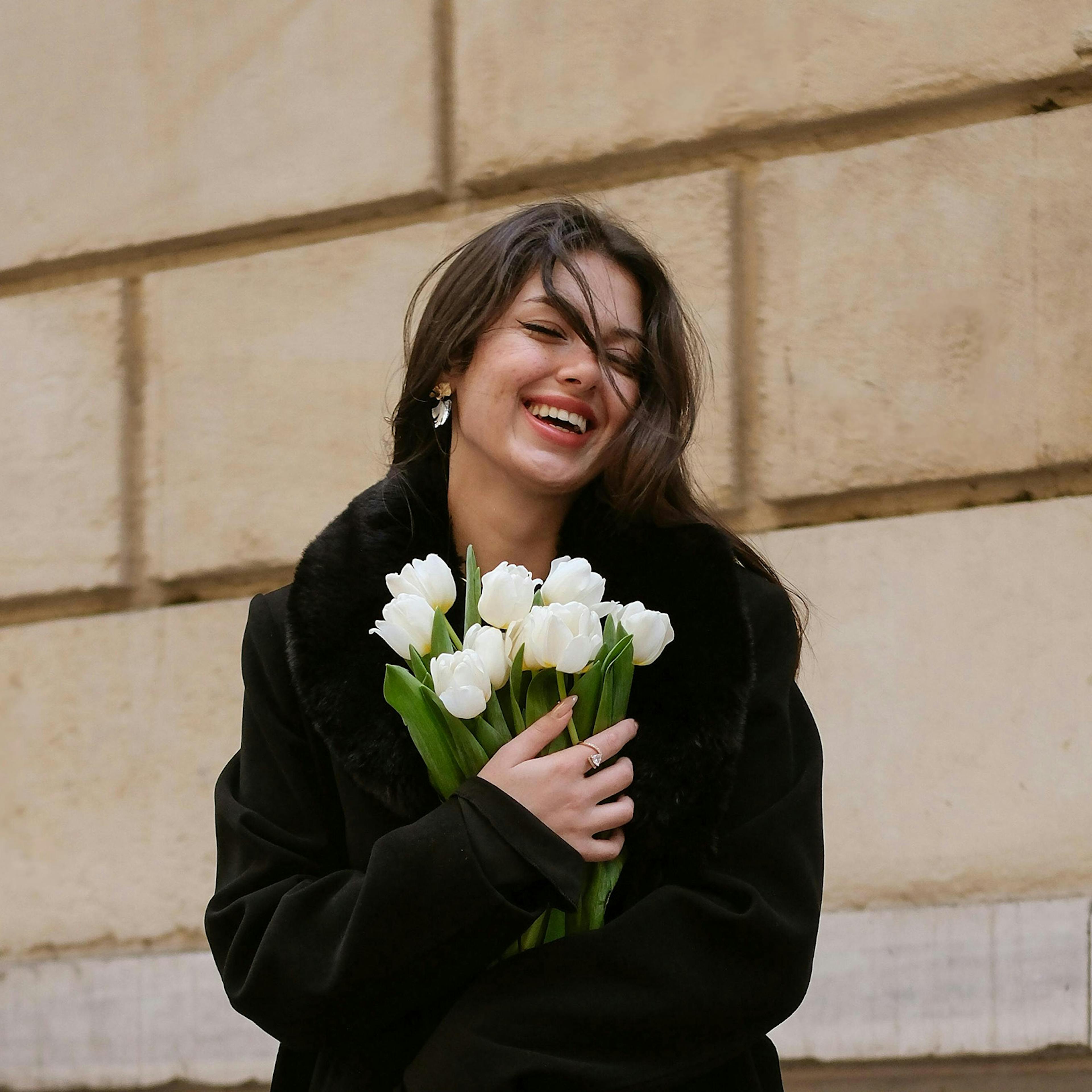 ragazza con cappotto nero che stringe sul petto un mazzo di tulipani