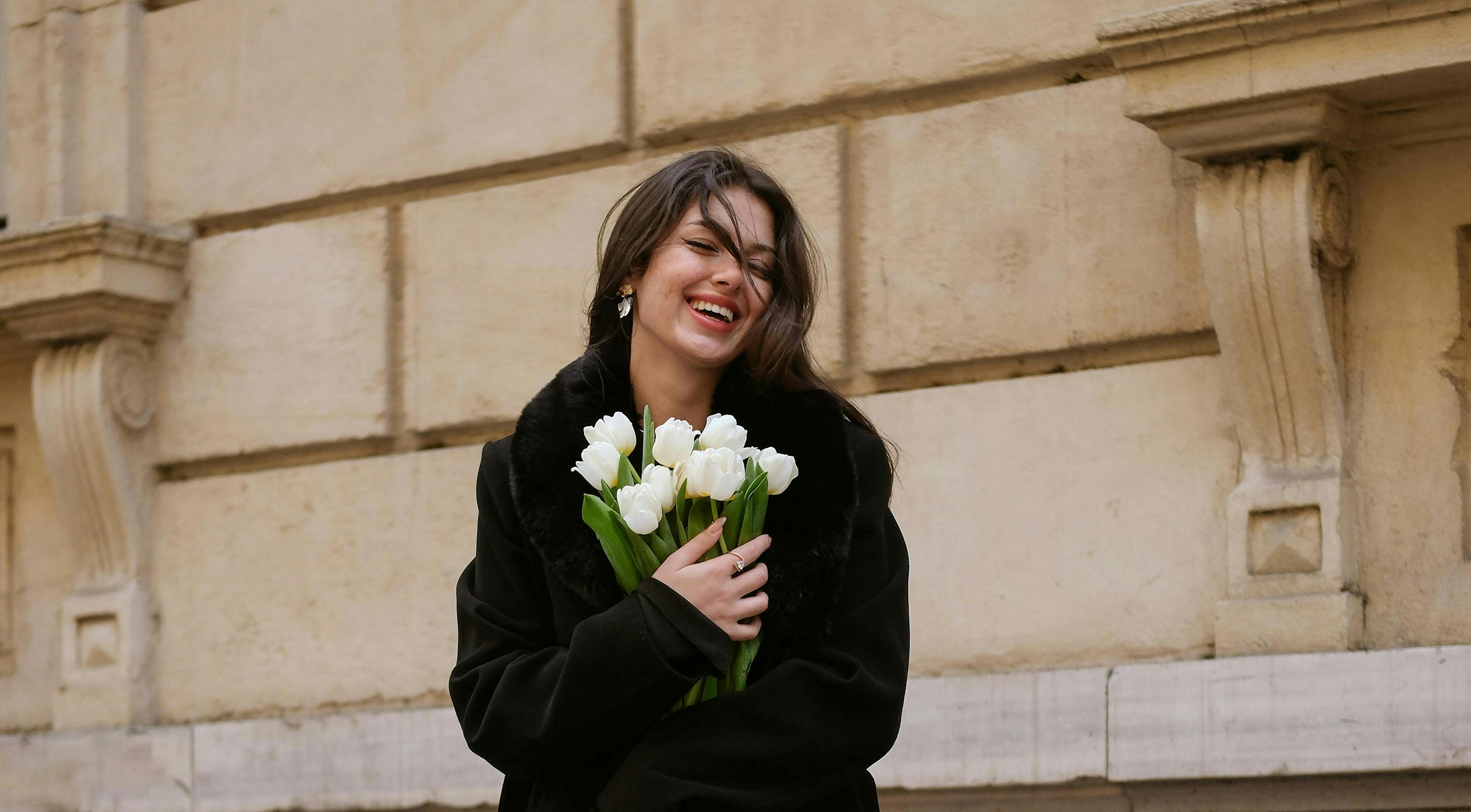 ragazza con cappotto nero che stringe sul petto un mazzo di tulipani