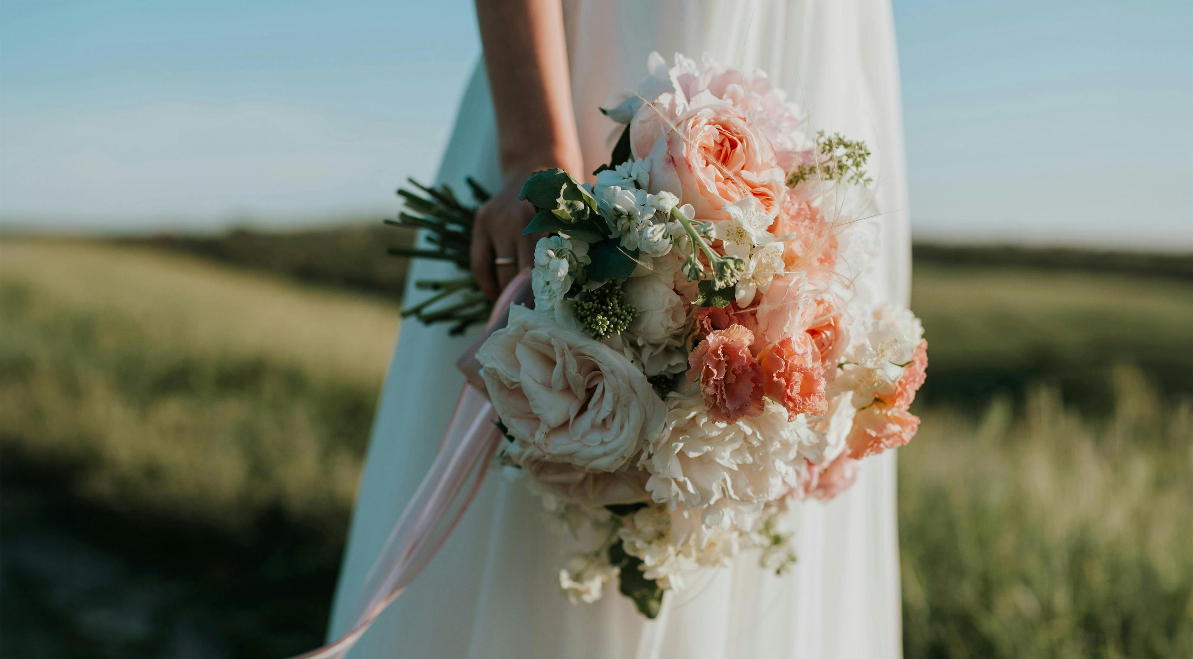 Sposa che tiene bouquet di fiori in un campo