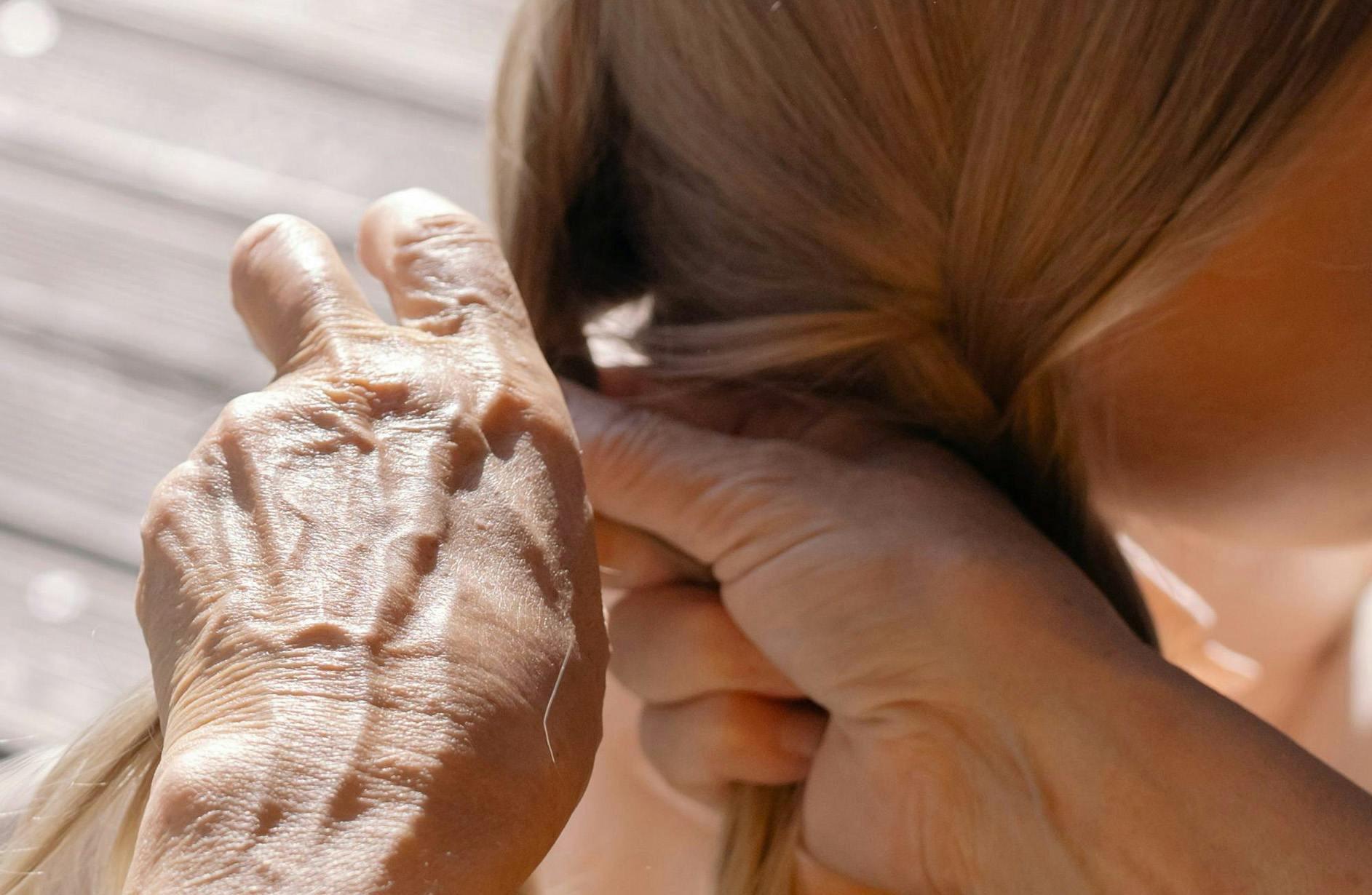 mani di anziano che fanno una treccia ad una bambina con capelli biondi