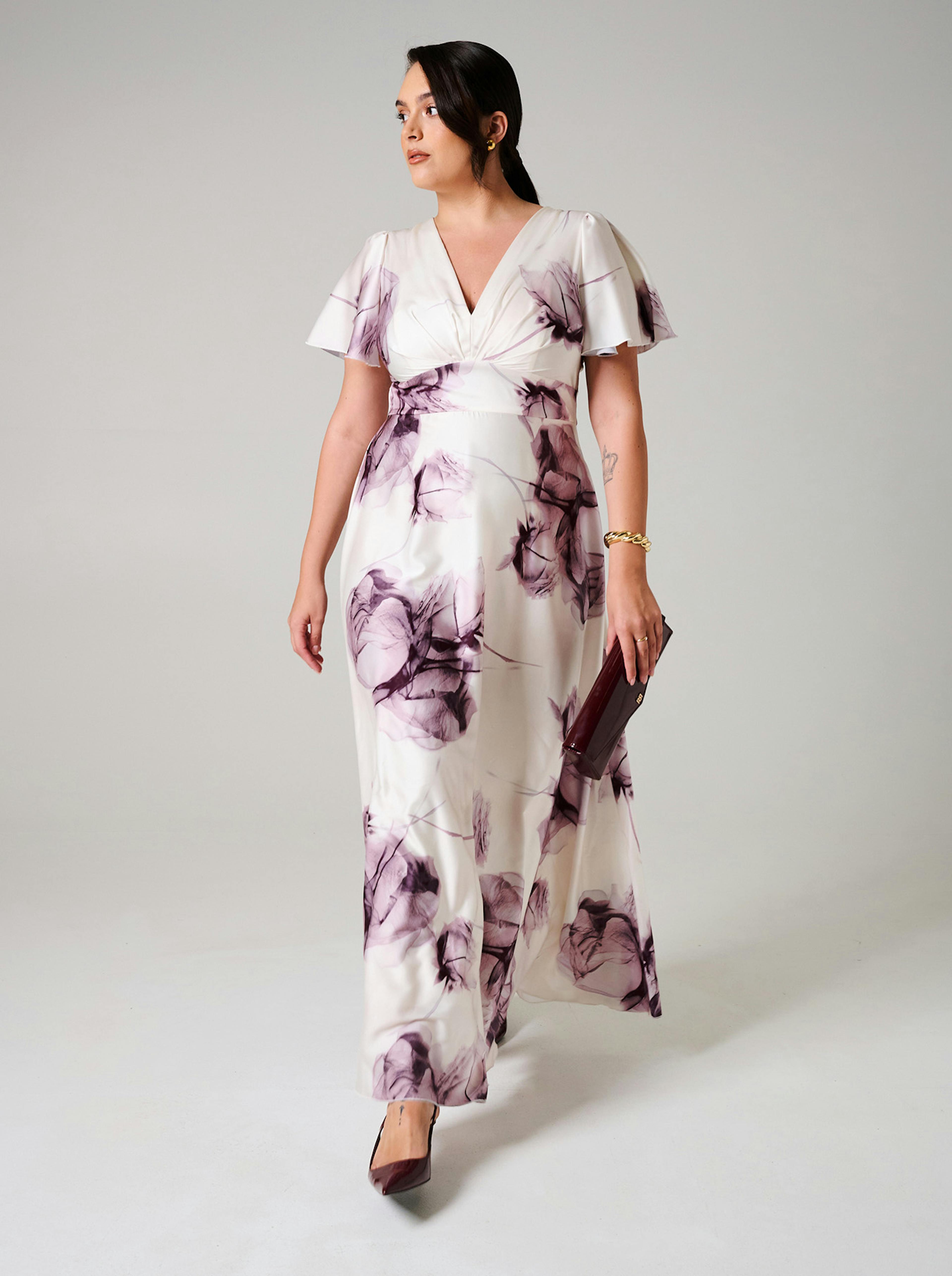 A curvy woman in a flowing white dress with purple floral patterns walks confidently. 