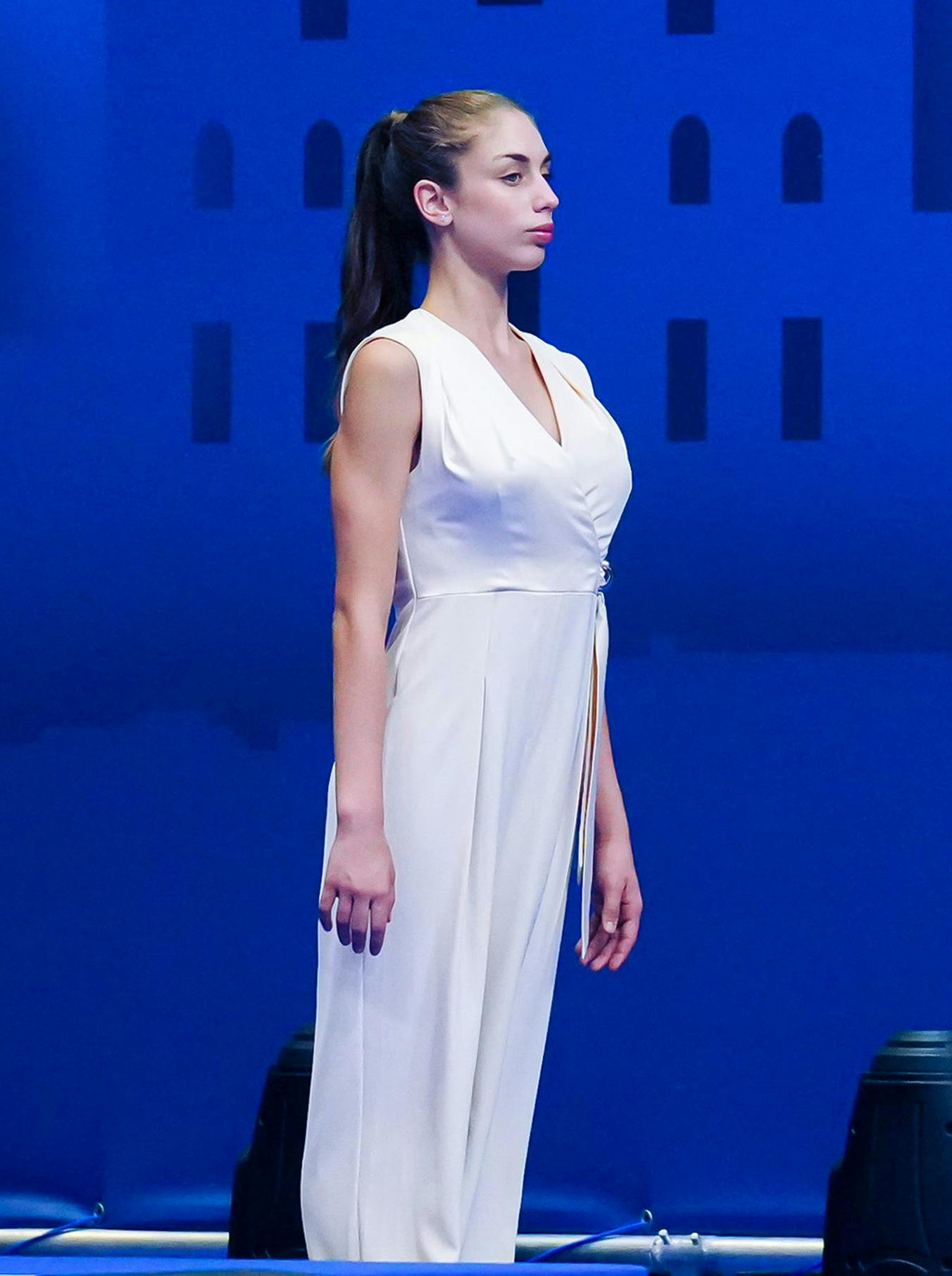 A woman in a white jumpsuit stands on a blue stage.