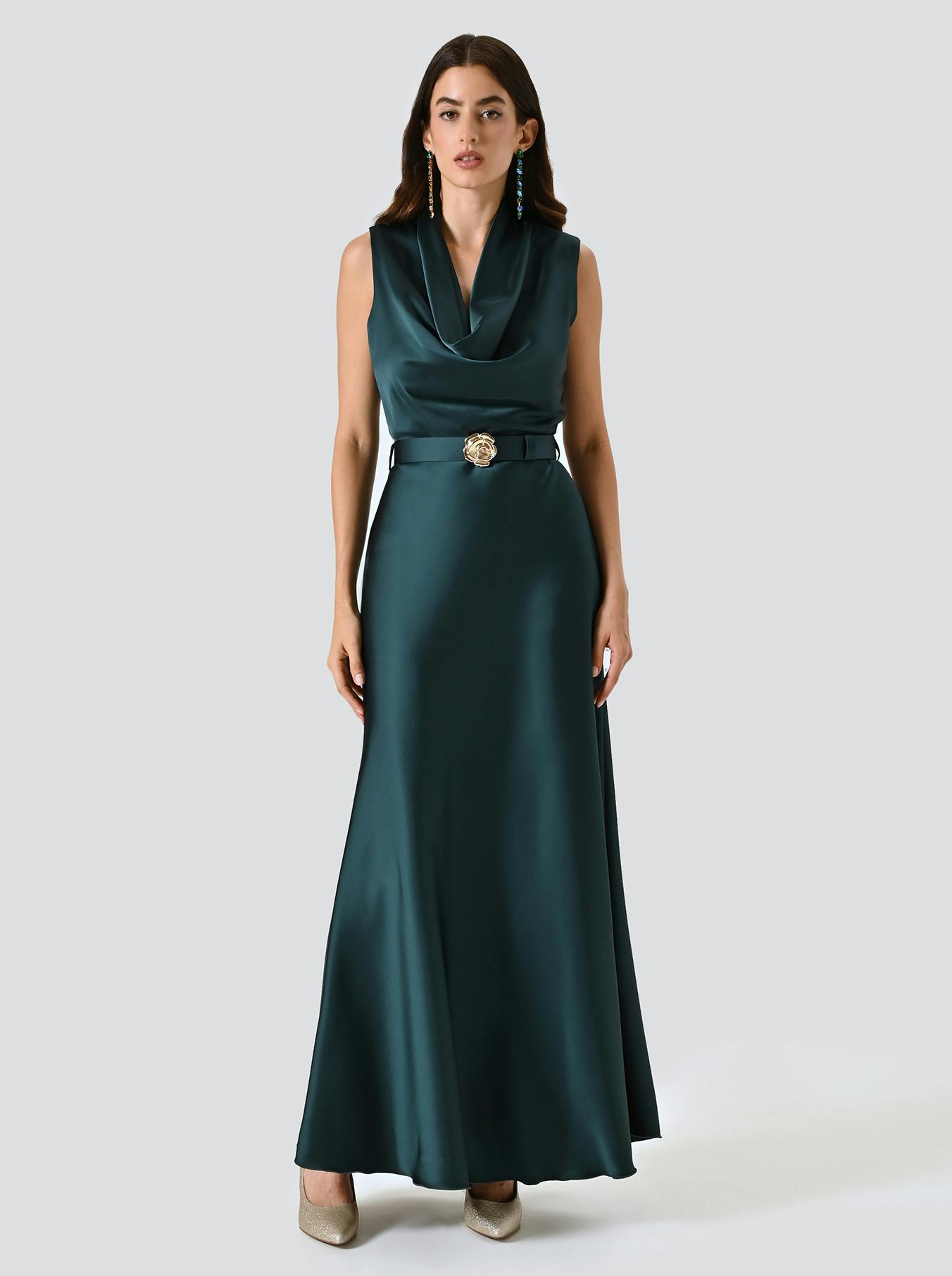 Woman in a sleeveless, teal satin gown with a cowl neckline and belt adorned with a floral buckle. The tone is elegant with a calm expression.
