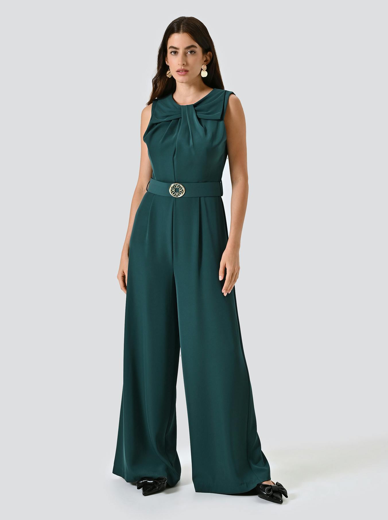Woman in a sleeveless, dark green jumpsuit with a belted waist and wide-legged pants.