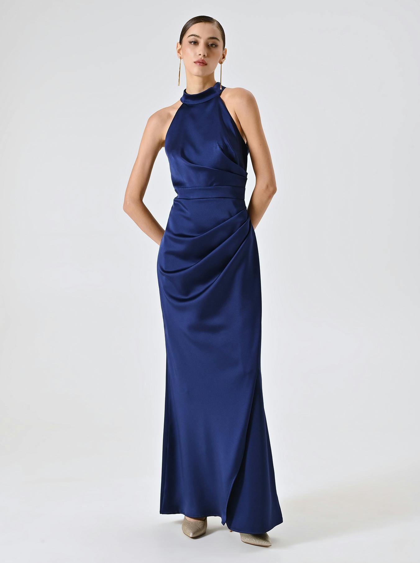 A person in a sleek, royal blue satin halter dress stands confidently against a plain background. The look is elegant and modern with a poised expression.