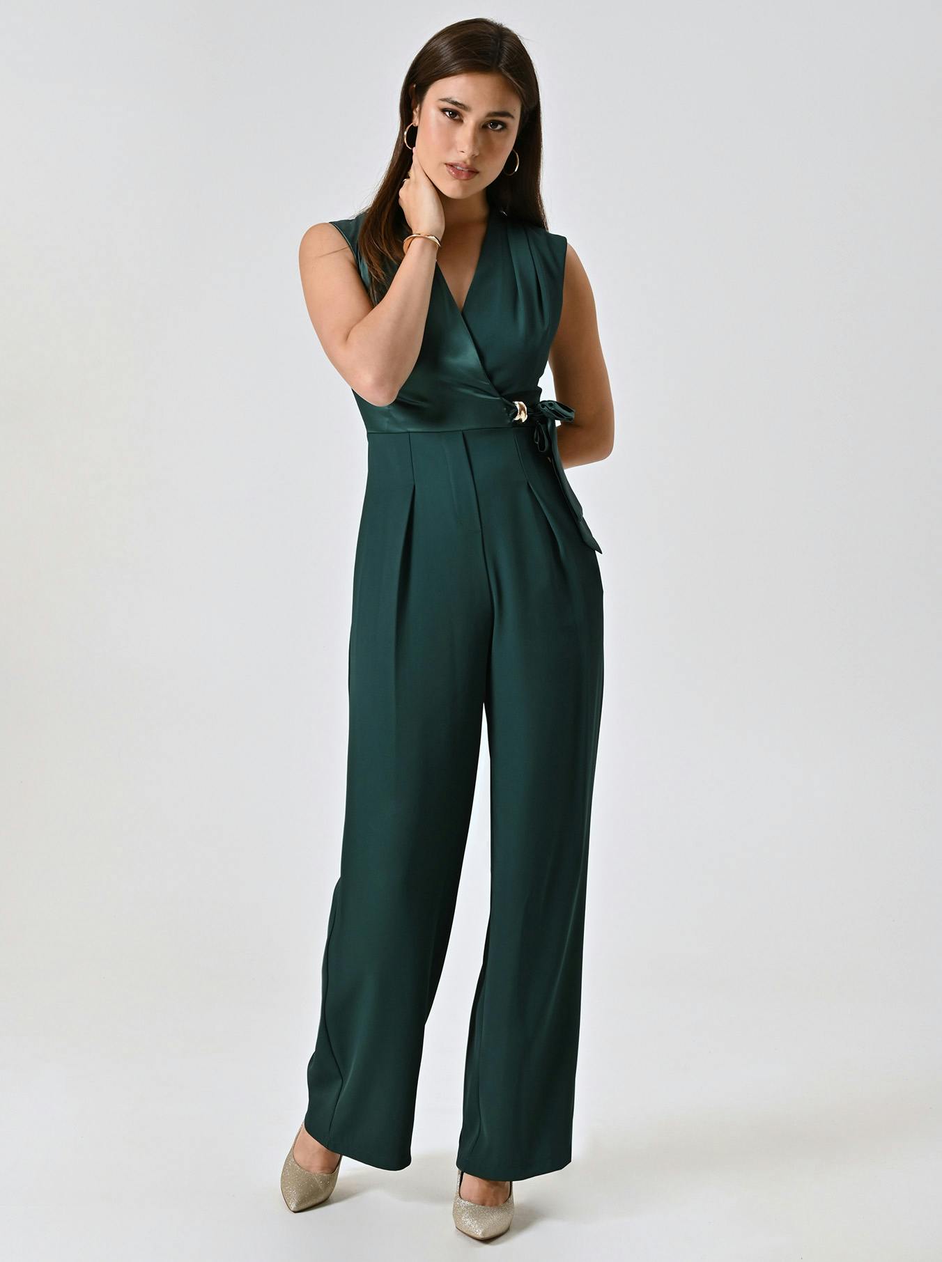 Woman in a stylish emerald green jumpsuit, with a V-neck and wide-leg pants, poses confidently against a neutral background, exuding elegance.