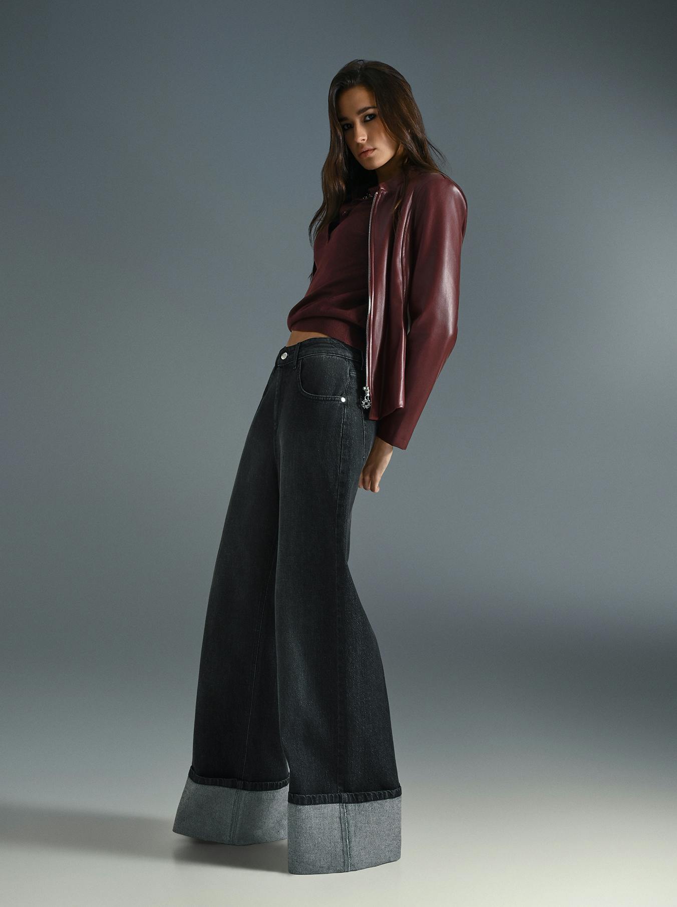 A woman wearing a burgundy top and wide denim jeans stands confidently, showcasing a casual yet stylish outfit.