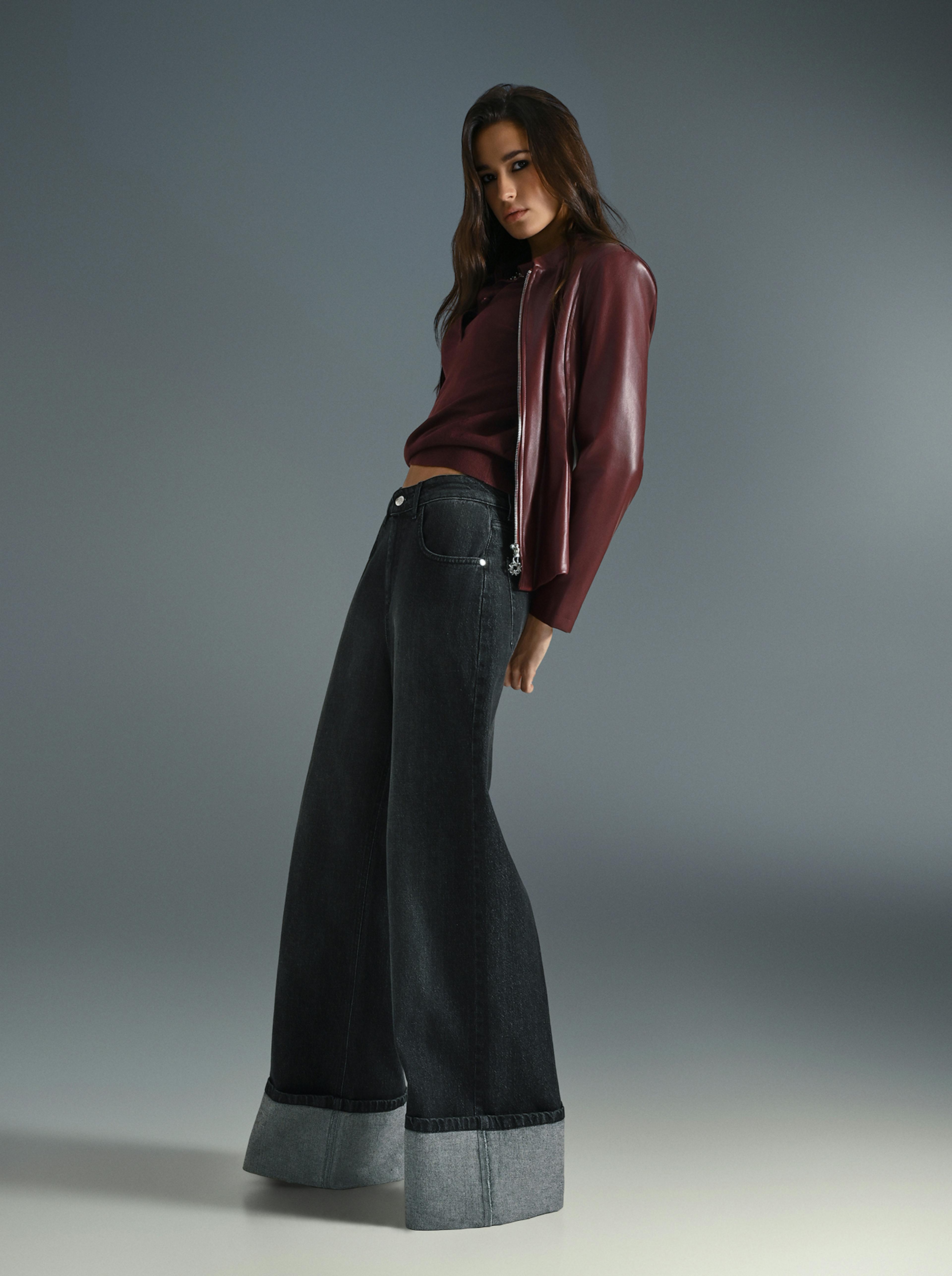 A woman wearing a burgundy top and wide denim jeans stands confidently, showcasing a casual yet stylish outfit.