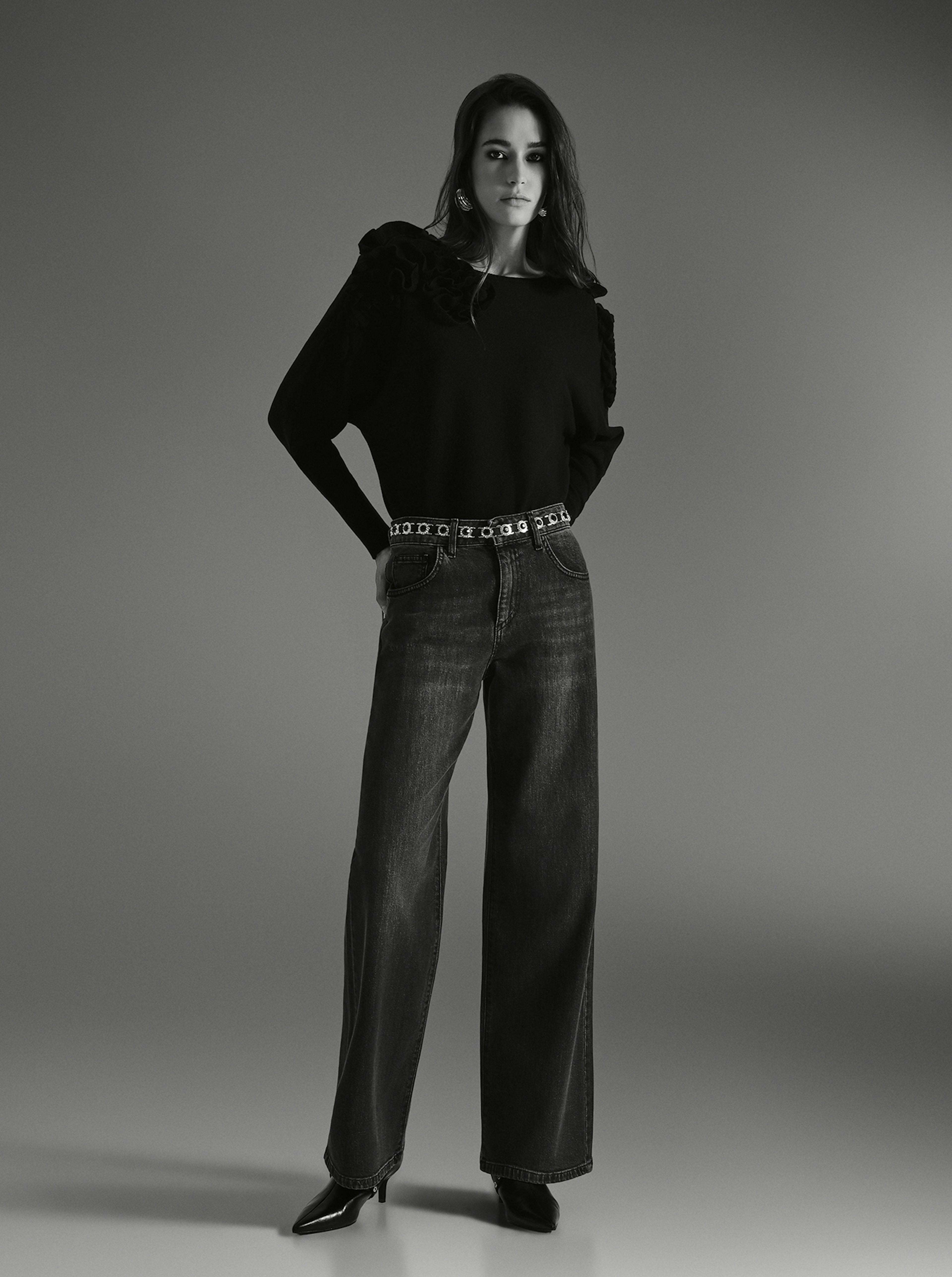 A black and white image of a woman in denim, striking a pose for the camera with a confident expression.