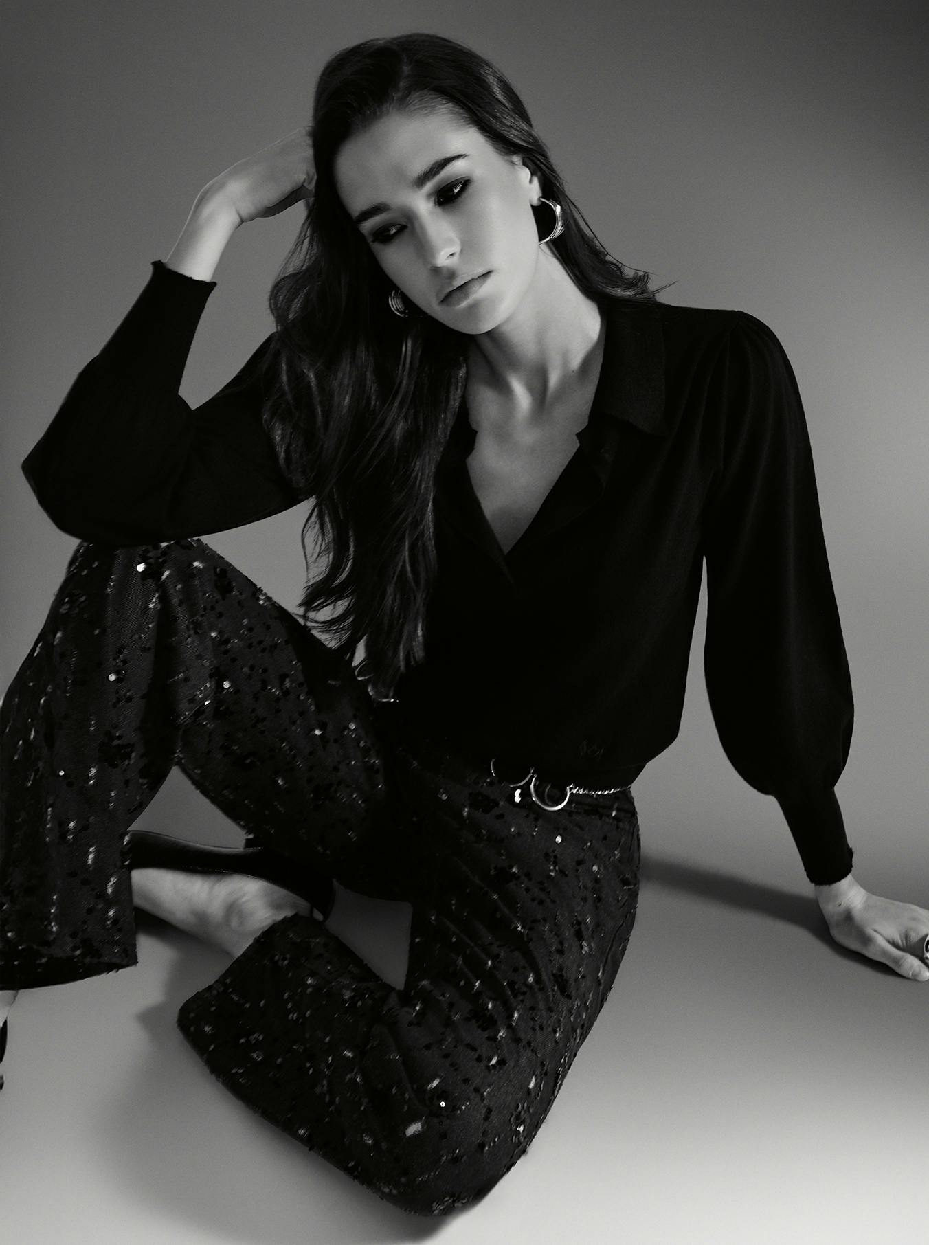 A woman in black and white denim sitting on the floor, looking contemplative and relaxed.
