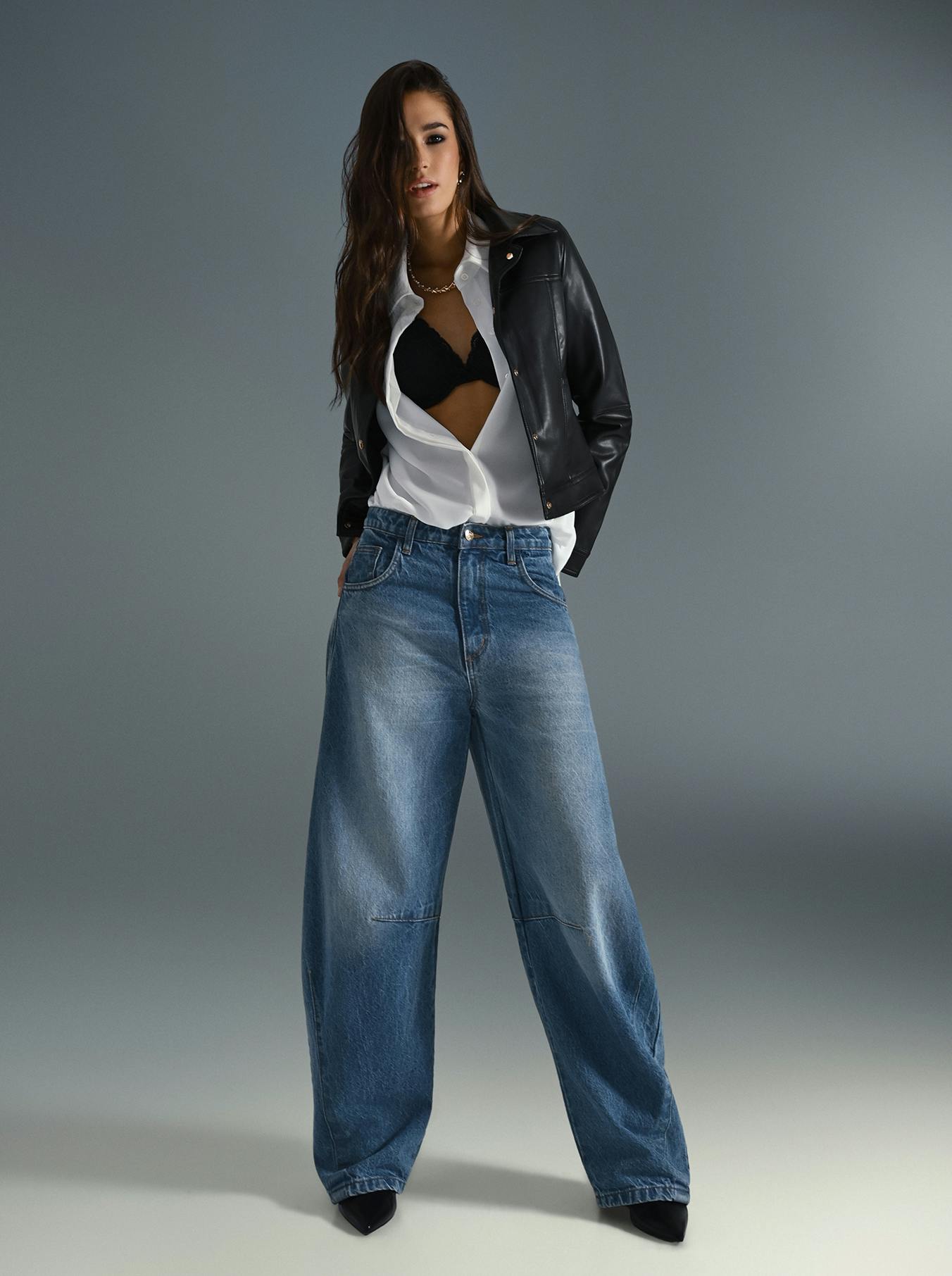 A woman wearing a leather jacket and wide jeans stands confidently, showcasing a stylish and casual outfit.