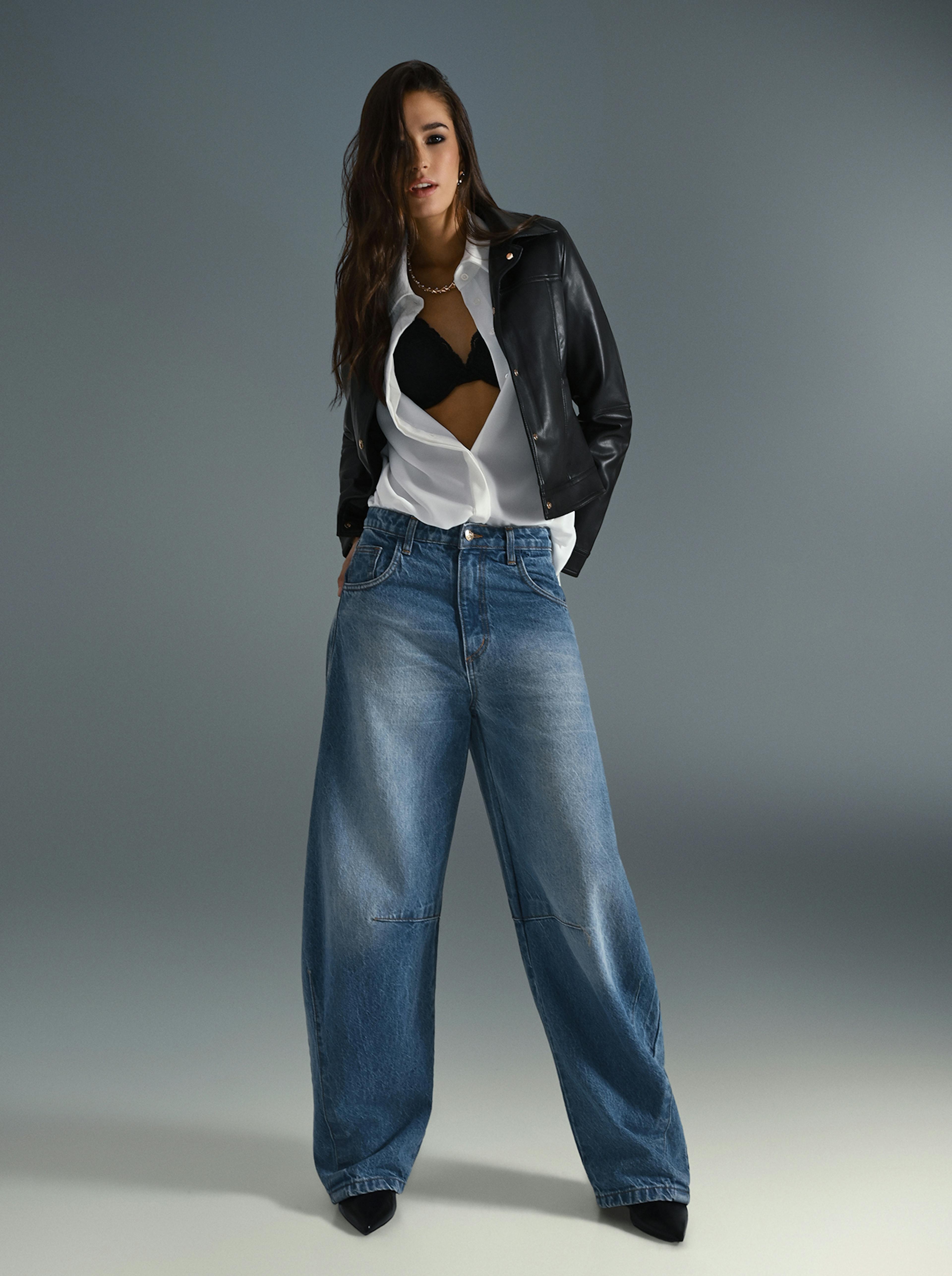 A woman wearing a leather jacket and wide jeans stands confidently, showcasing a stylish and casual outfit.