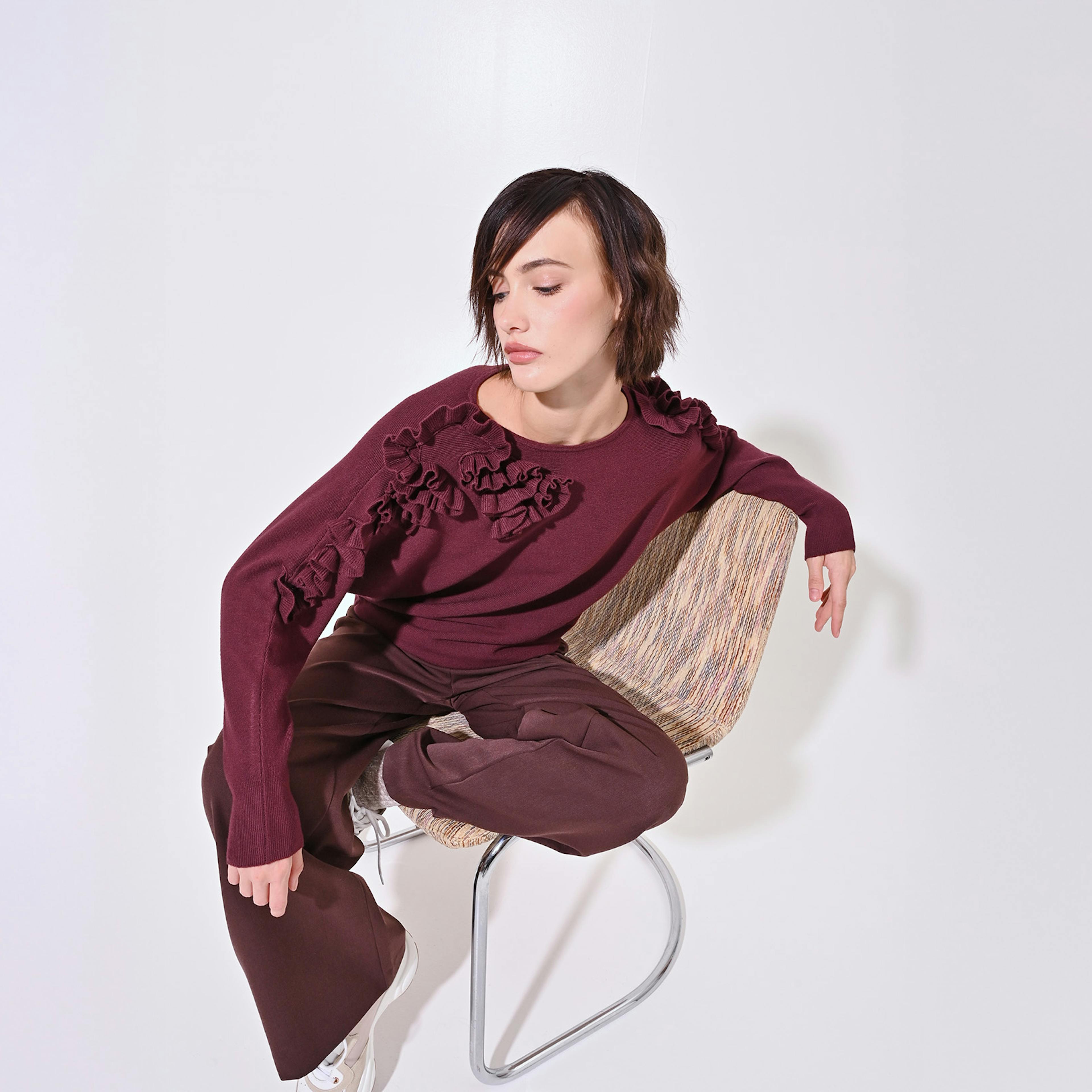 A person in a burgundy sweater with floral patterns sits on a modern chair against a white background, conveying a calm and contemplative mood.
