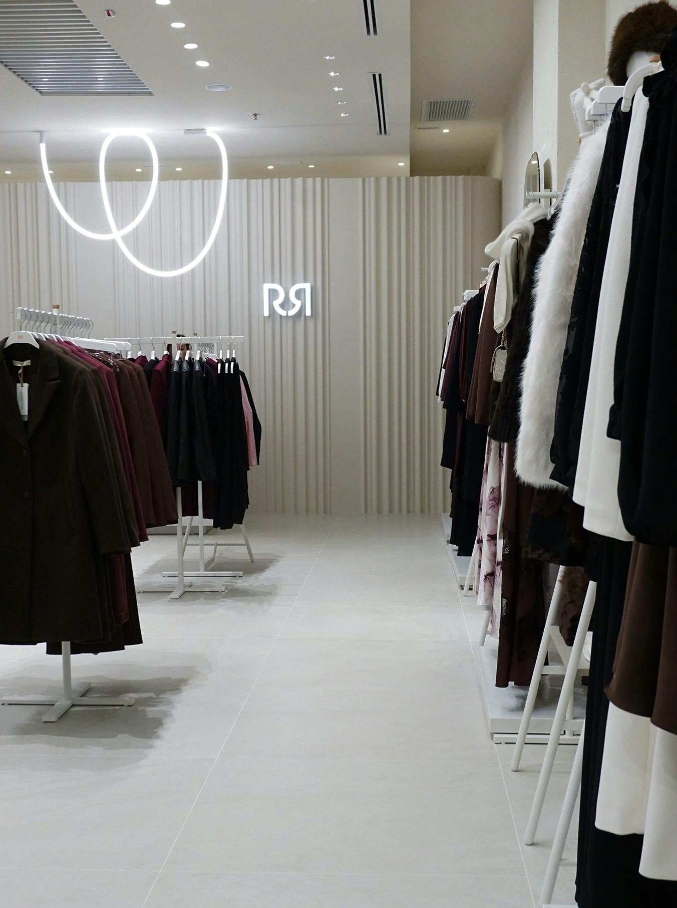 Minimalist clothing store with neutral tones and elegant coats on racks. Modern lighting and signage create a sleek, sophisticated ambiance.