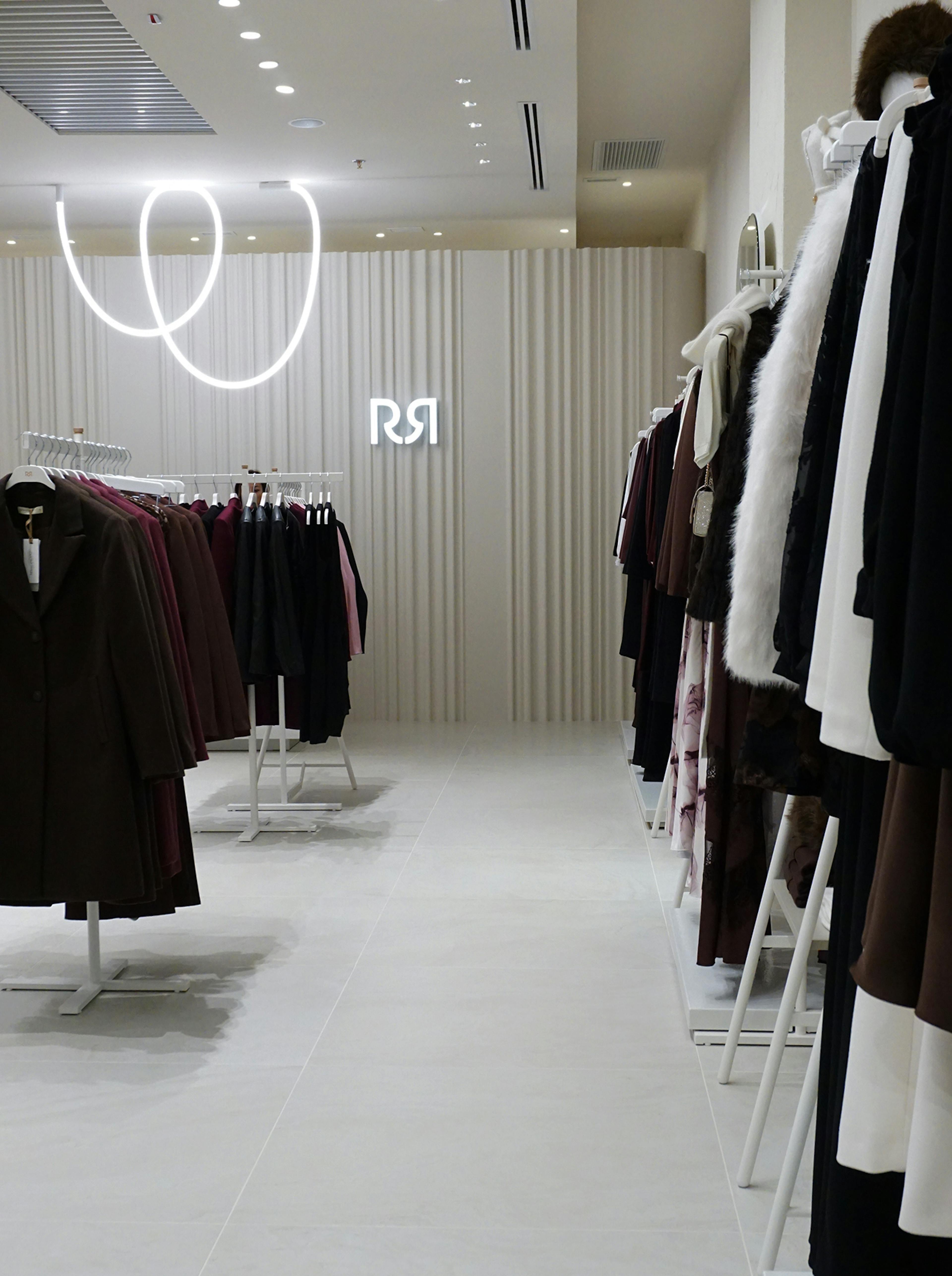Minimalist clothing store with neutral tones and elegant coats on racks. Modern lighting and signage create a sleek, sophisticated ambiance.