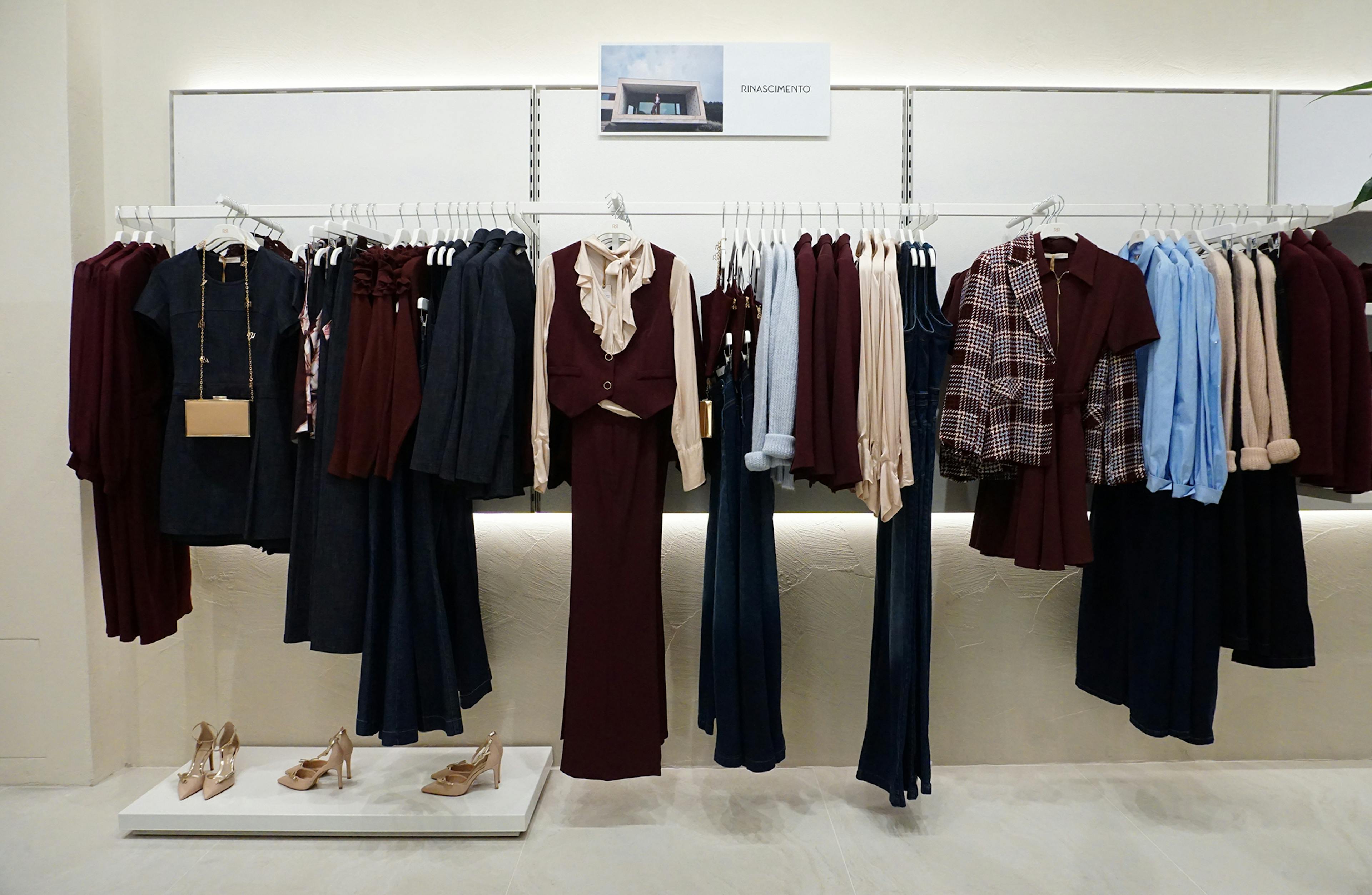 Clothing display with maroon, beige, and blue outfits on hangers. Elegant and sophisticated setting with high heels on a light floor.