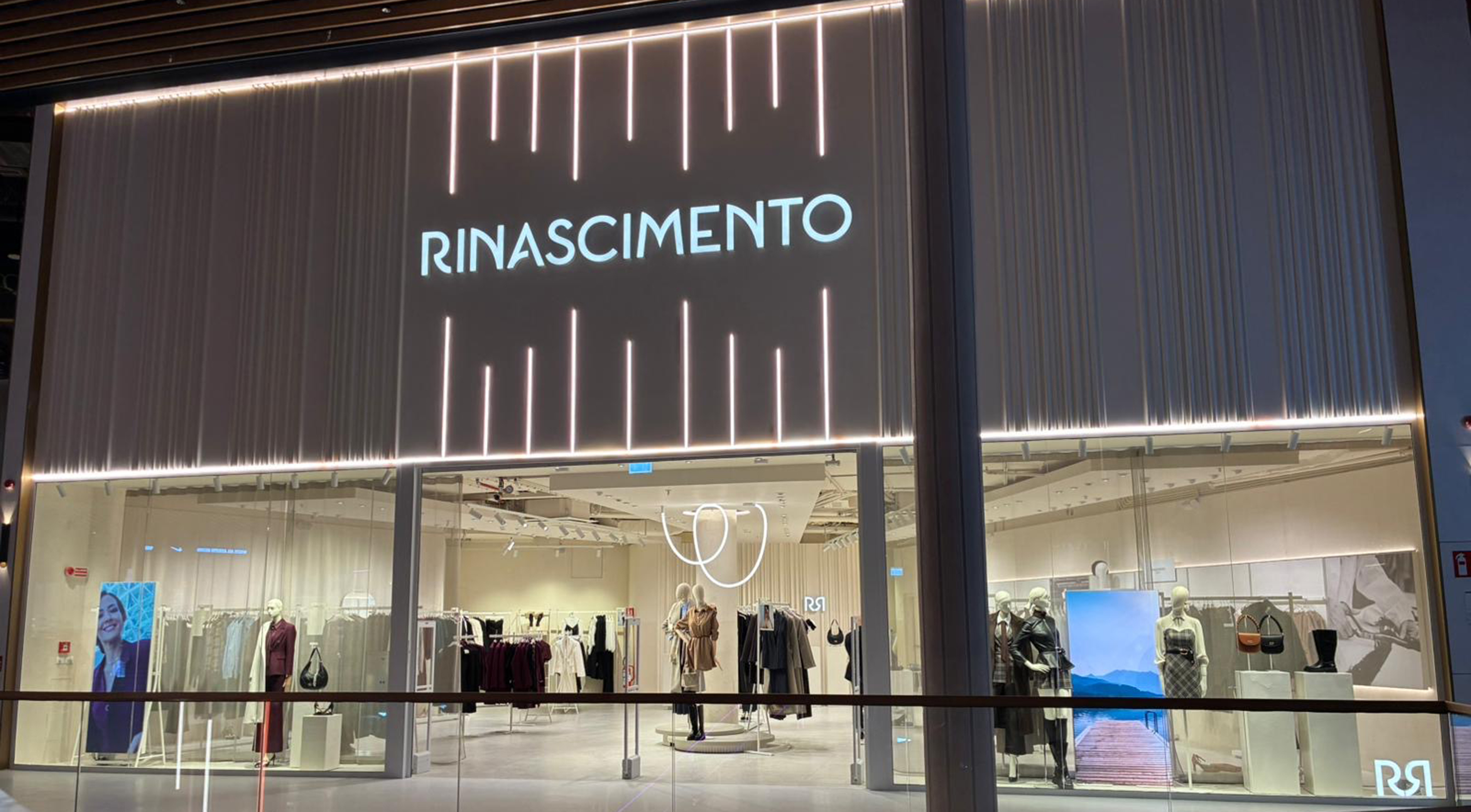 Storefront of a modern clothing shop named "Rinascimento" with a sleek logo. The interior displays elegant garments and accessories under soft lighting.