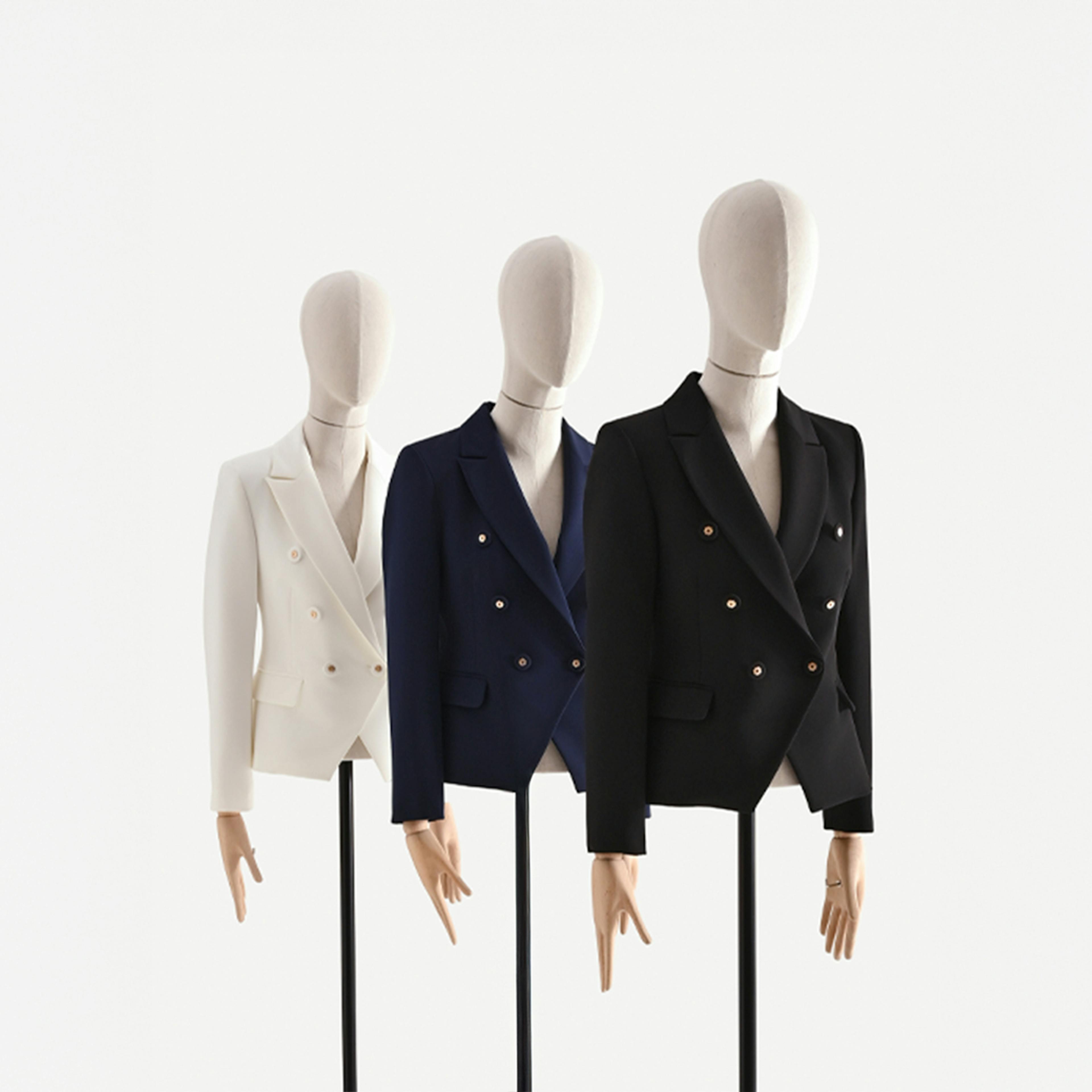 Three mannequins in a row display double-breasted blazers: white, navy, and black. The minimalist, clean setup conveys elegance and style.