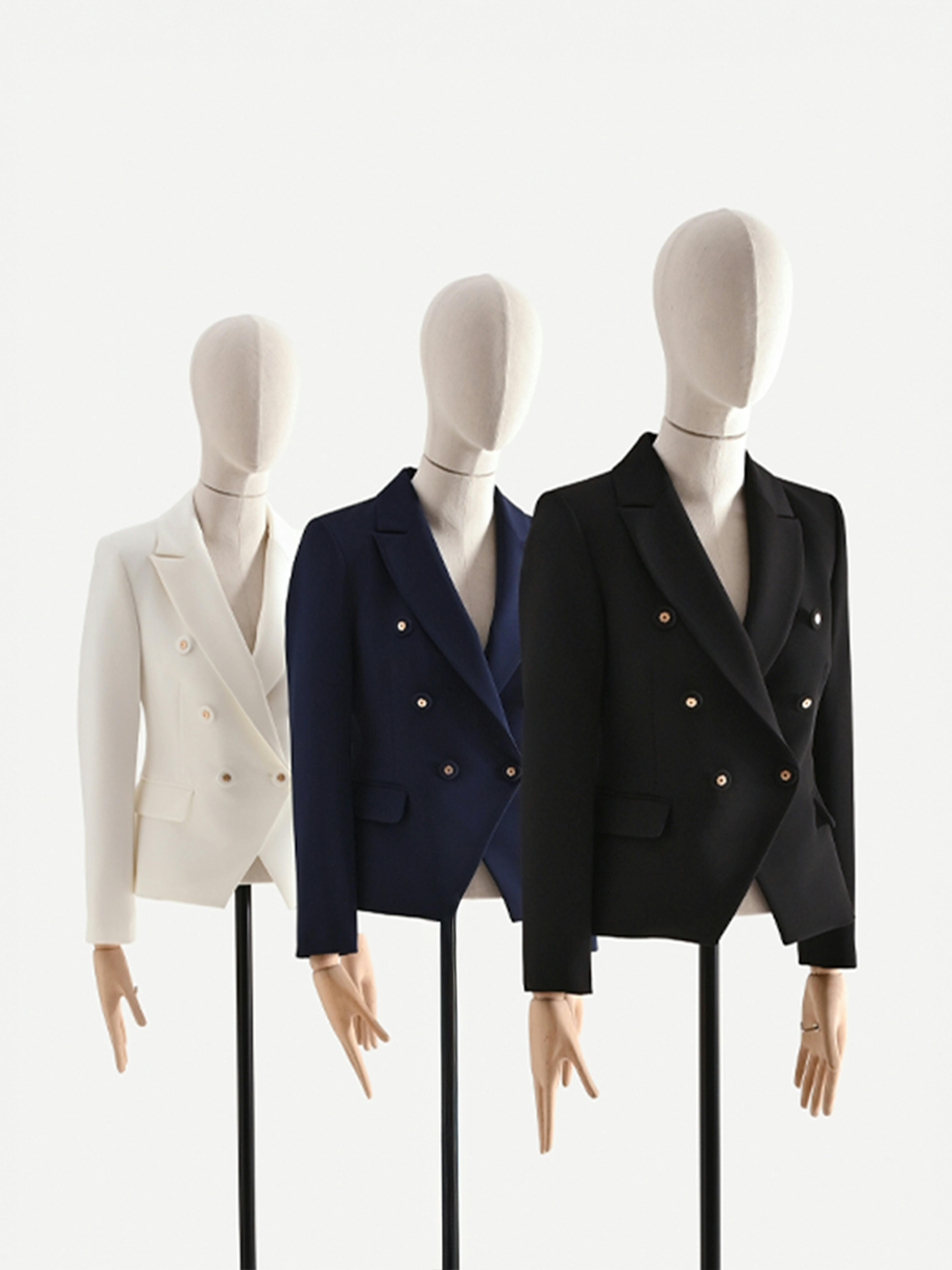 Three mannequins in a row display double-breasted blazers: white, navy, and black. The minimalist, clean setup conveys elegance and style.