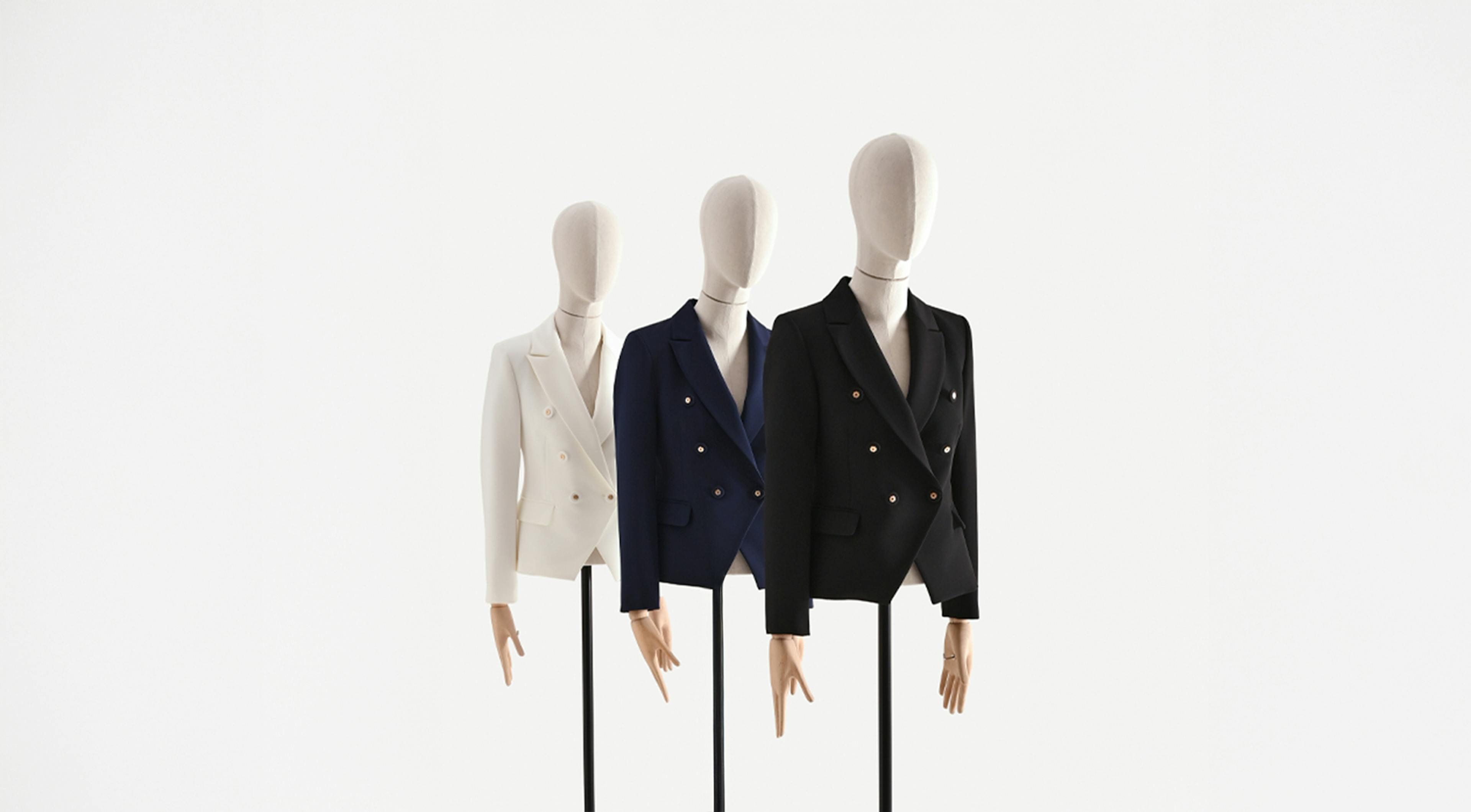 Three mannequins in a row display double-breasted blazers: white, navy, and black. The minimalist, clean setup conveys elegance and style.