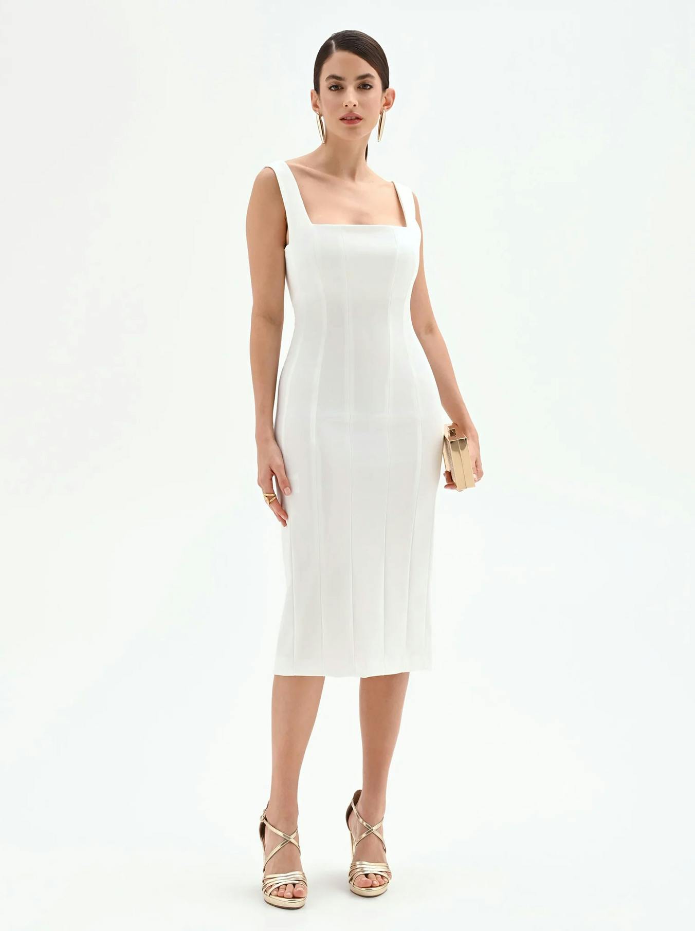 Woman in a sleek, sleeveless white midi dress and gold heels stands confidently holding a small clutch. Minimalistic, elegant, and poised.