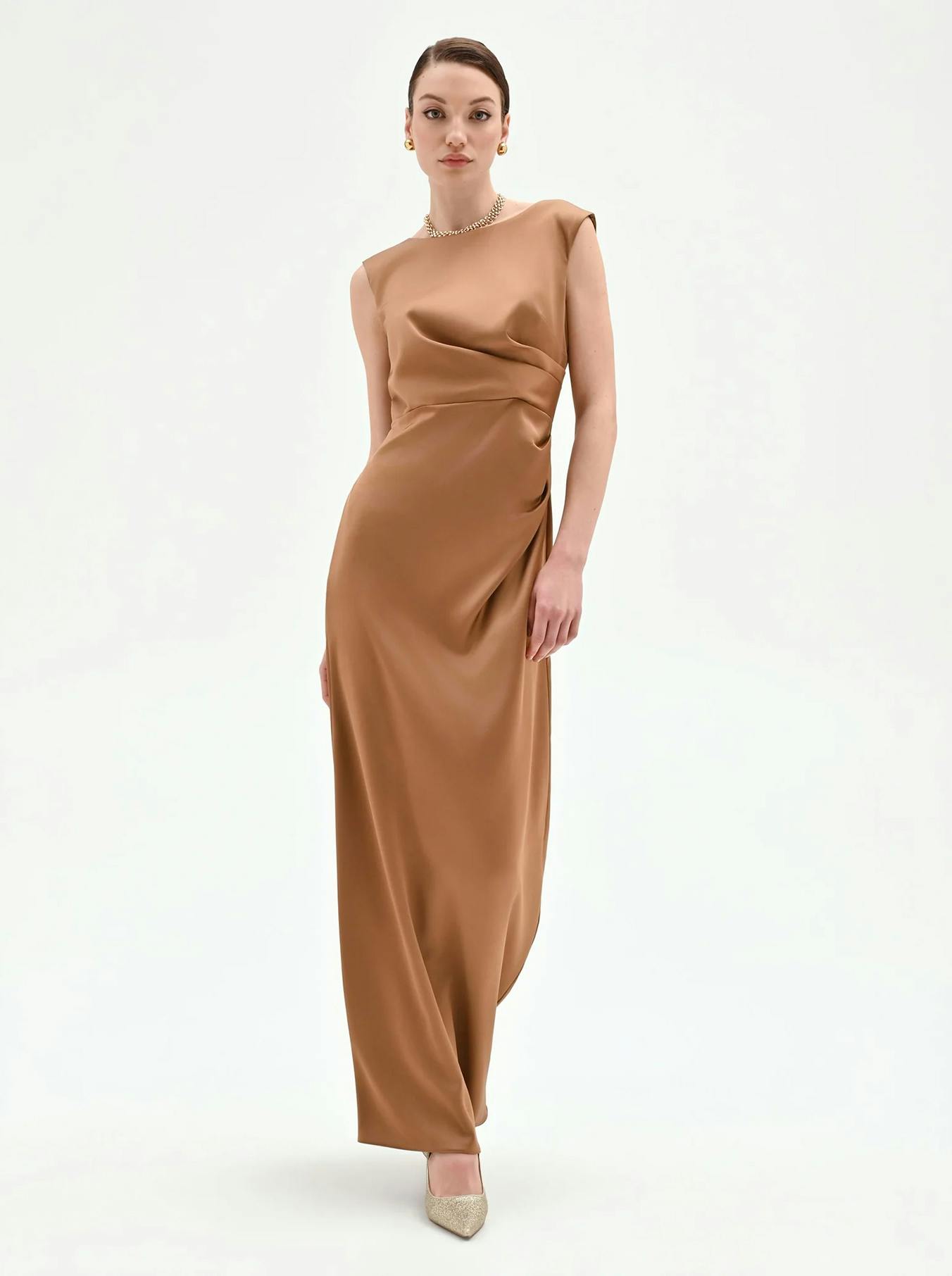 A model poses elegantly in a sleek, brown satin dress, complemented by sparkling high heels against a minimalist background.