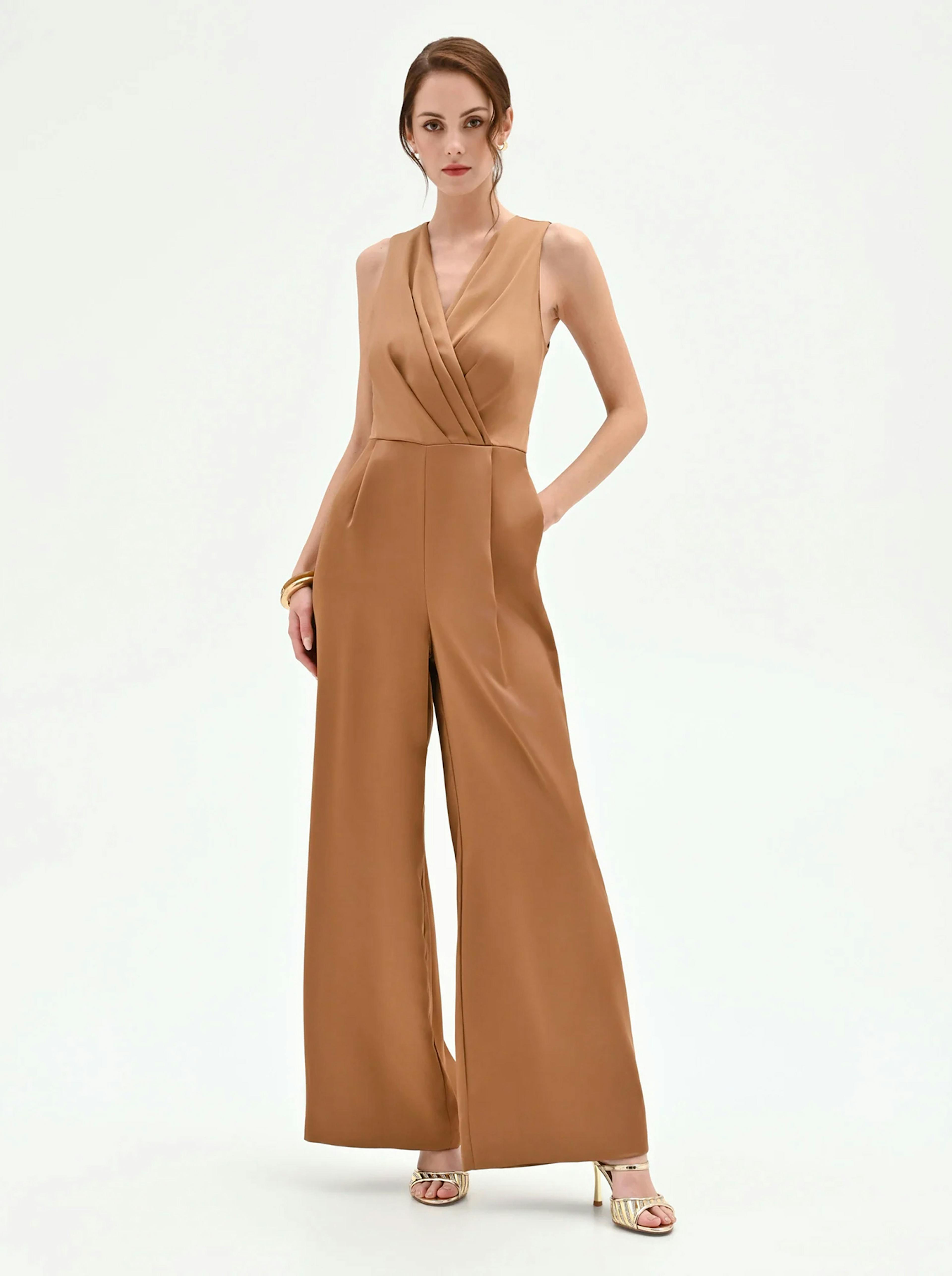 A model poses in a chic, sleeveless brown jumpsuit with a deep v-neck and wide legs, paired with stylish high-heeled sandals.