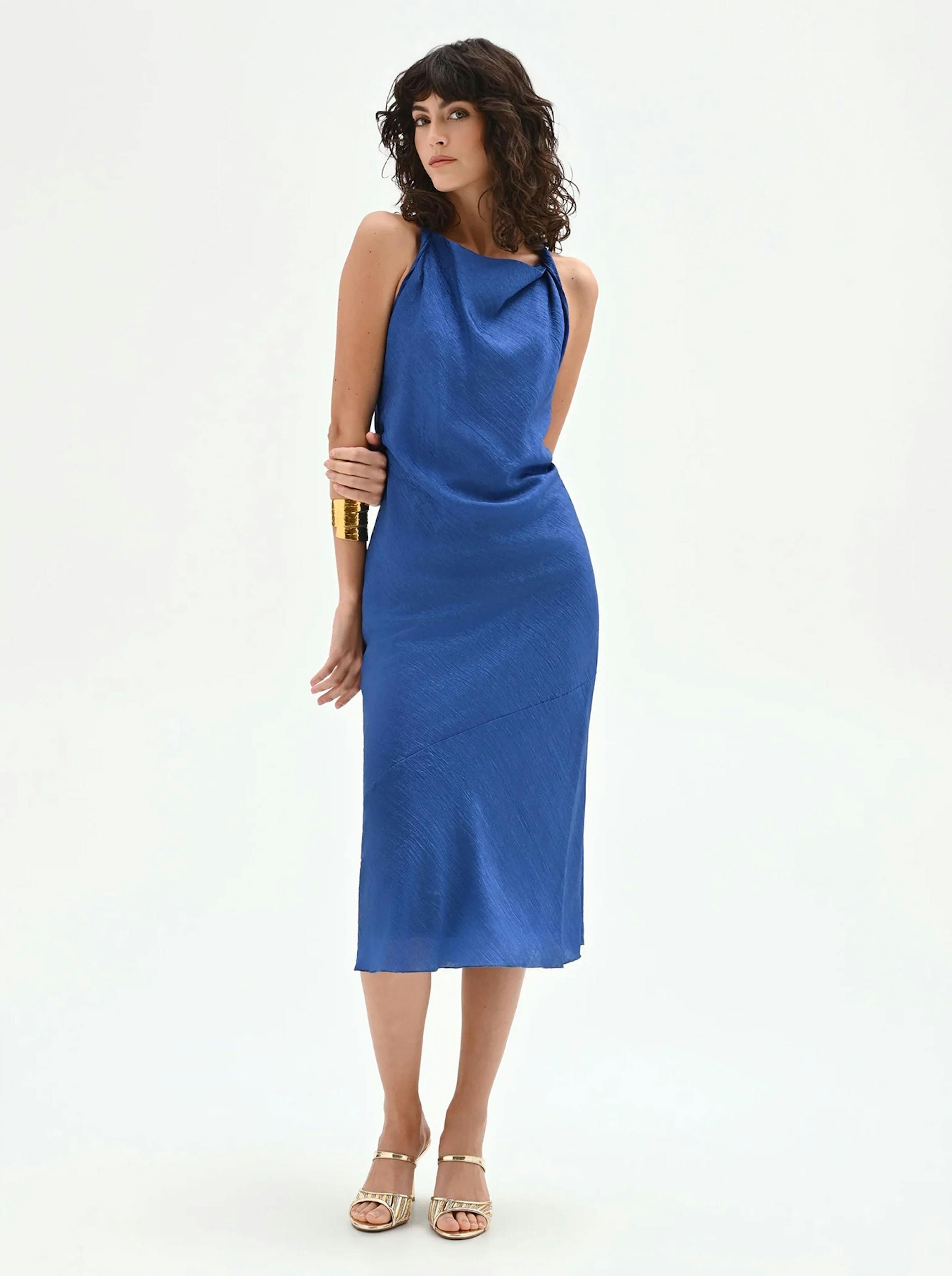 Royal blue midi slip dress in a shimmering textured satin fabric. Featuring a sophisticated draped cowl neckline and a sleeveless silhouette, styled with gold cuff jewelry and metallic sandals.