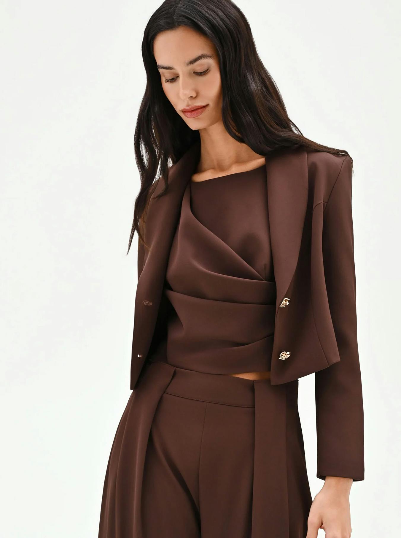 Modern chocolate brown women's suit featuring a cropped open blazer and a matching draped asymmetric top. A minimalist and trendy earthy-toned ensemble for high-fashion office wear or autumn events.