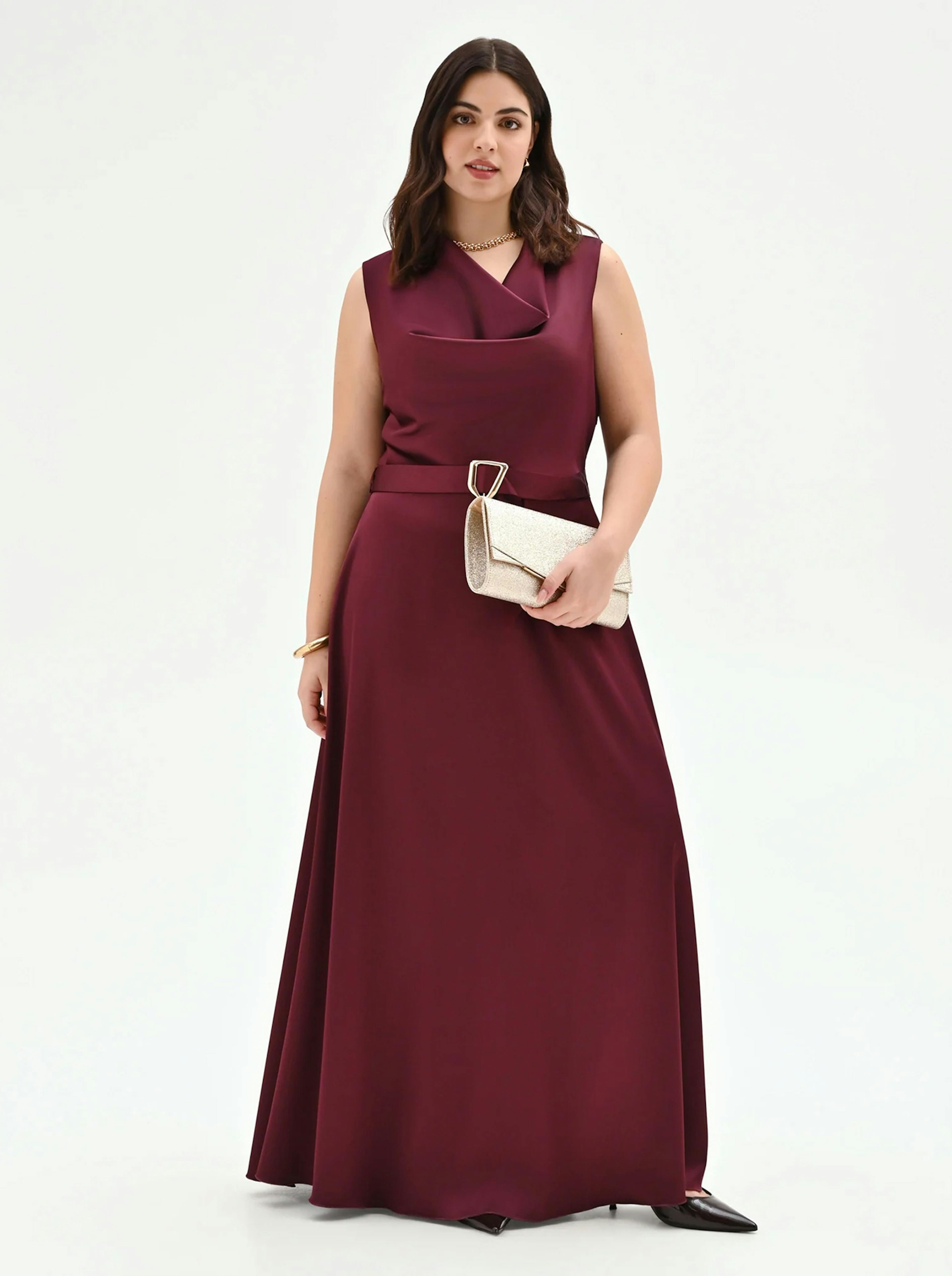 Elegant burgundy sleeveless maxi dress with a sophisticated cowl neckline and a matching belted waist. This satin-finish evening gown is perfect for formal galas or winter wedding guests. Styled with a gold glitter clutch.