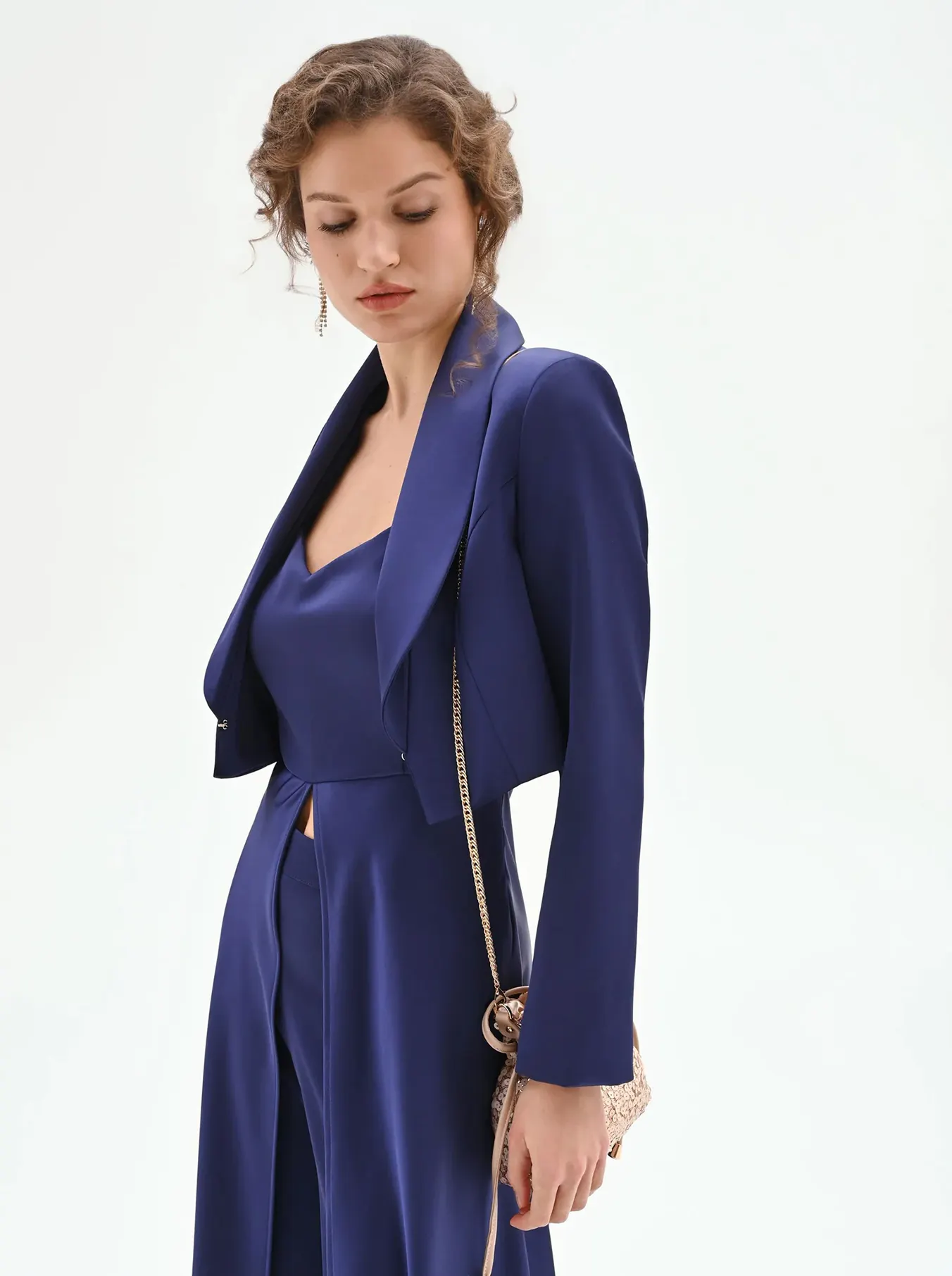 Model in a stylish navy blue suit with a cropped jacket, paired with a small metallic handbag, set against a plain white background.