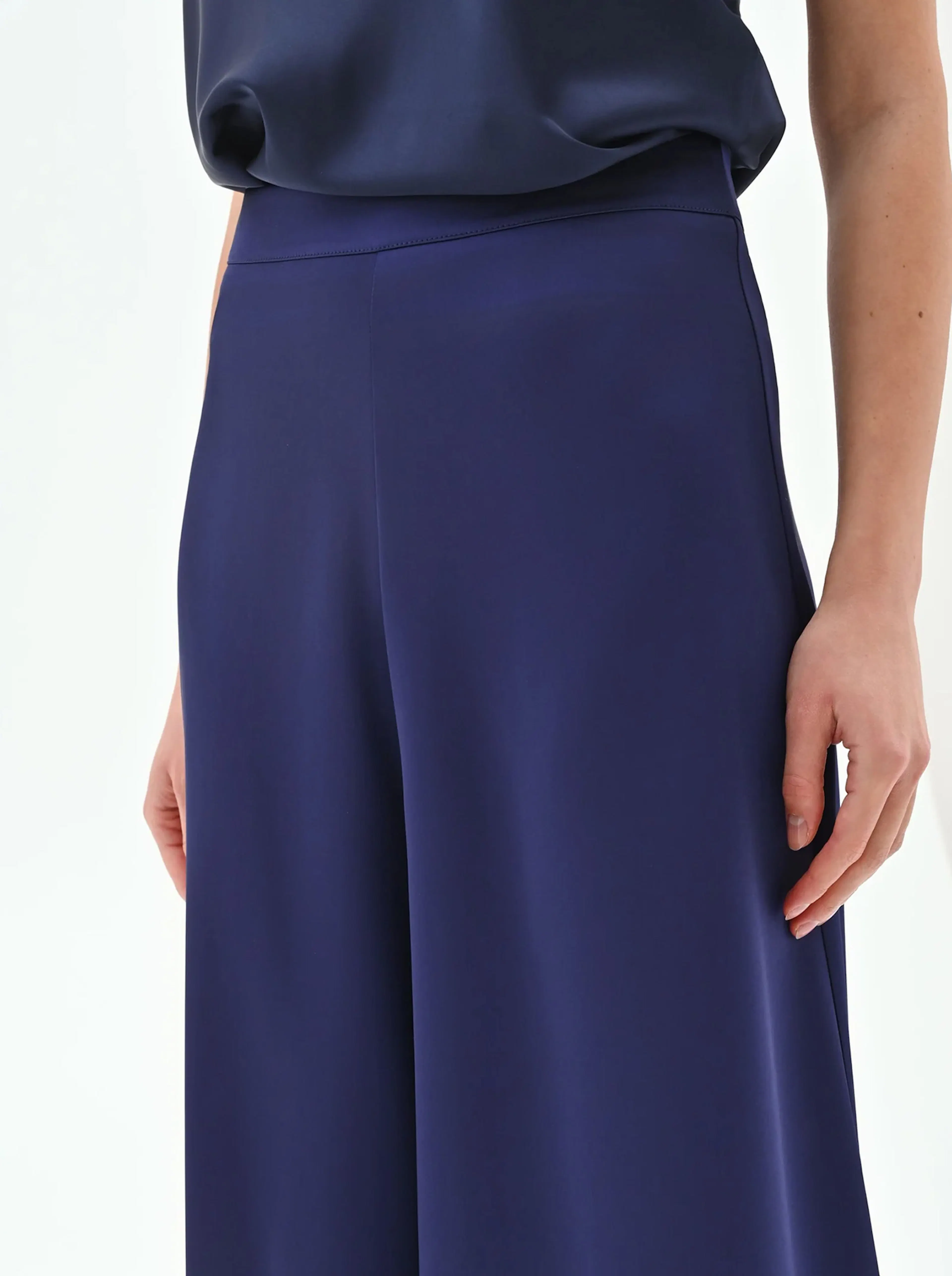 Close-up of a woman's navy blue trousers, highlighting the smooth fabric and wide-leg design, paired with a loose top.