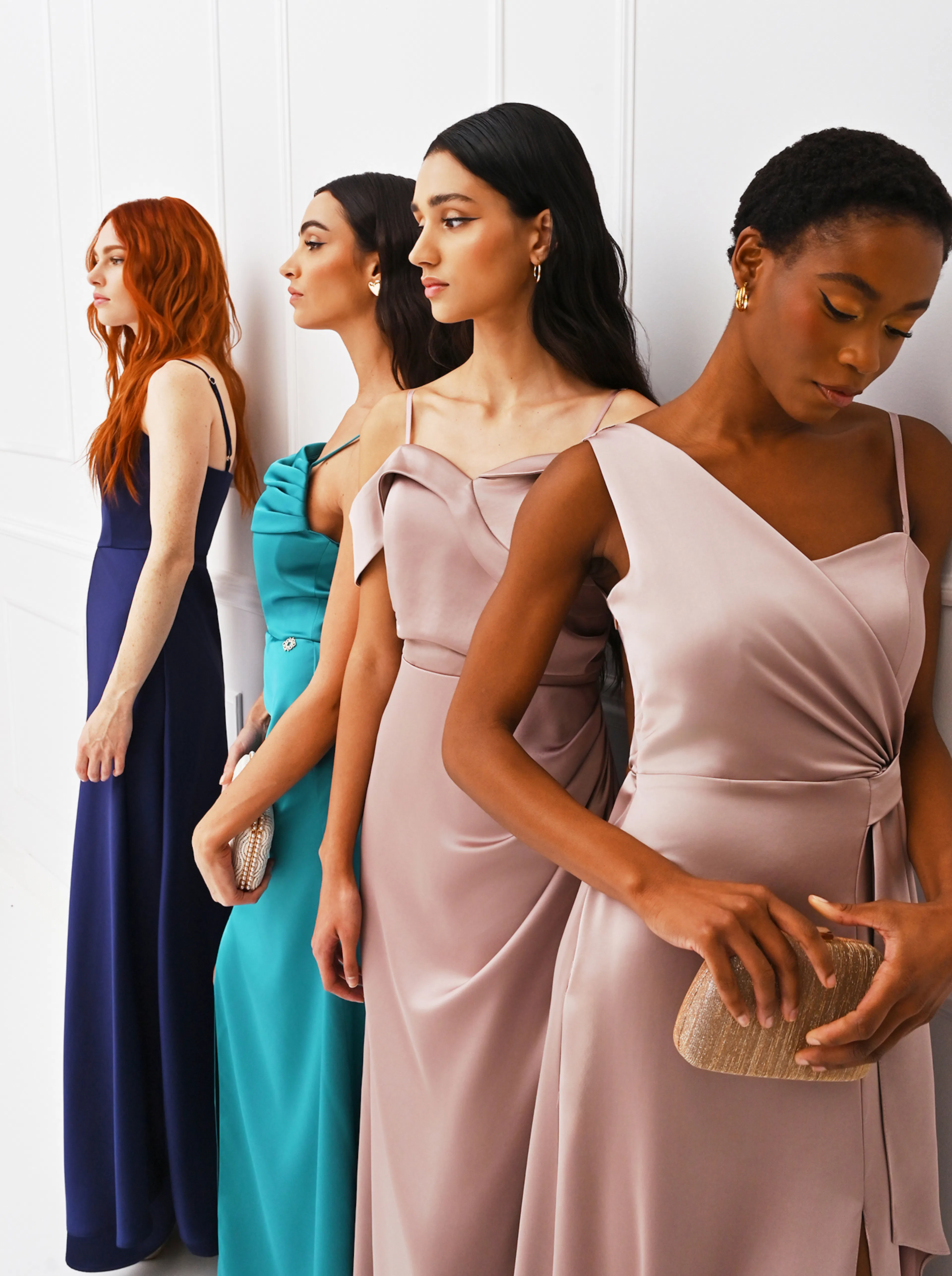 Four women stand in elegant dresses, showcasing diverse styles and colors against a clean, white backdrop.