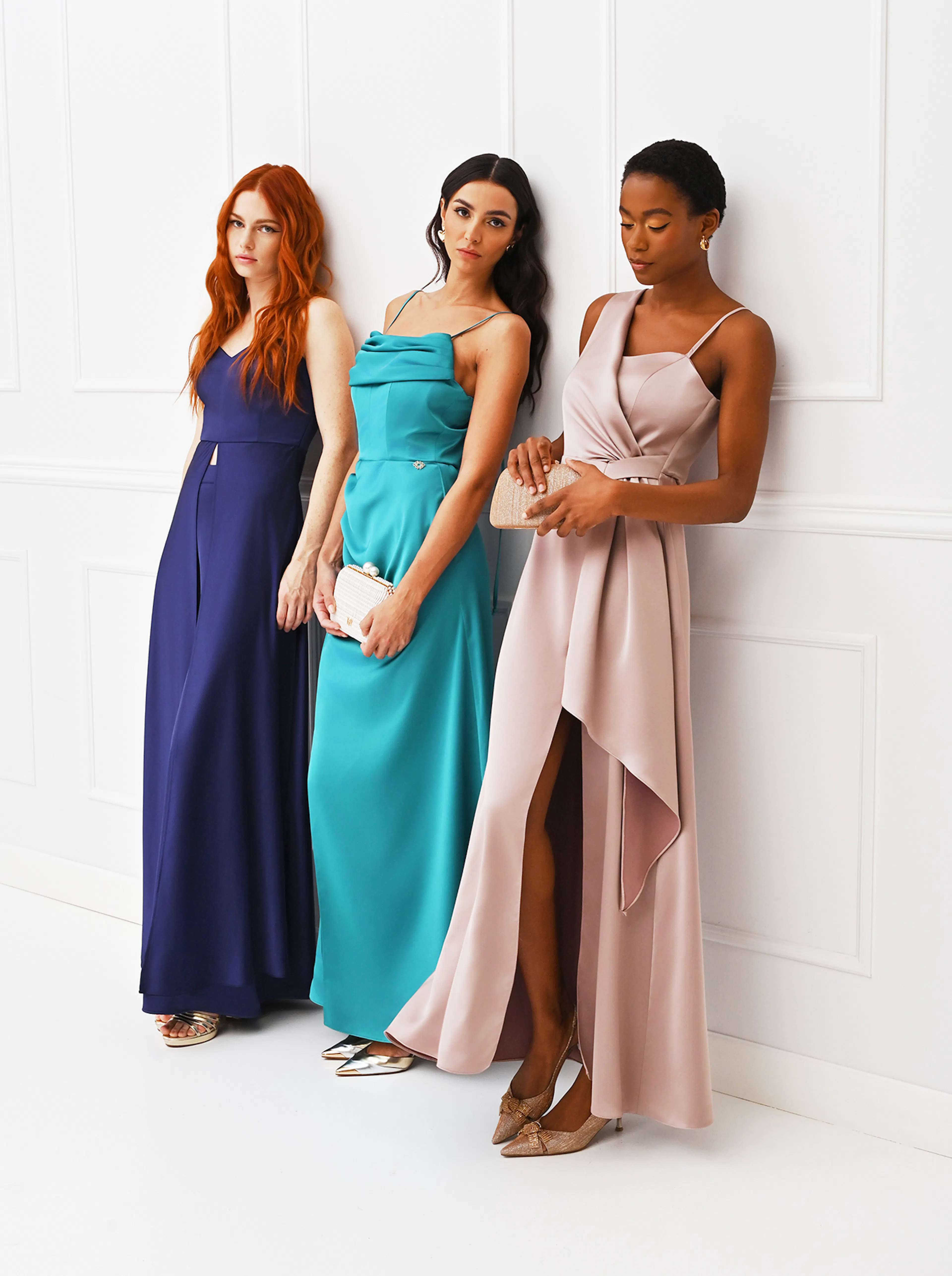 Three women stand in elegant dresses, showcasing diverse styles and colors against a clean, white backdrop.