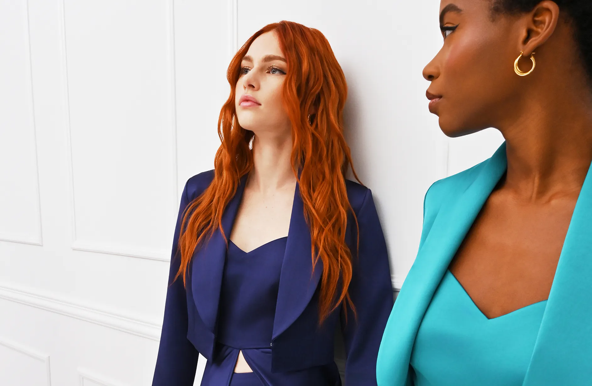 A person stands in a stylish navy blue gown with a cutout detail, against a bright white wall.