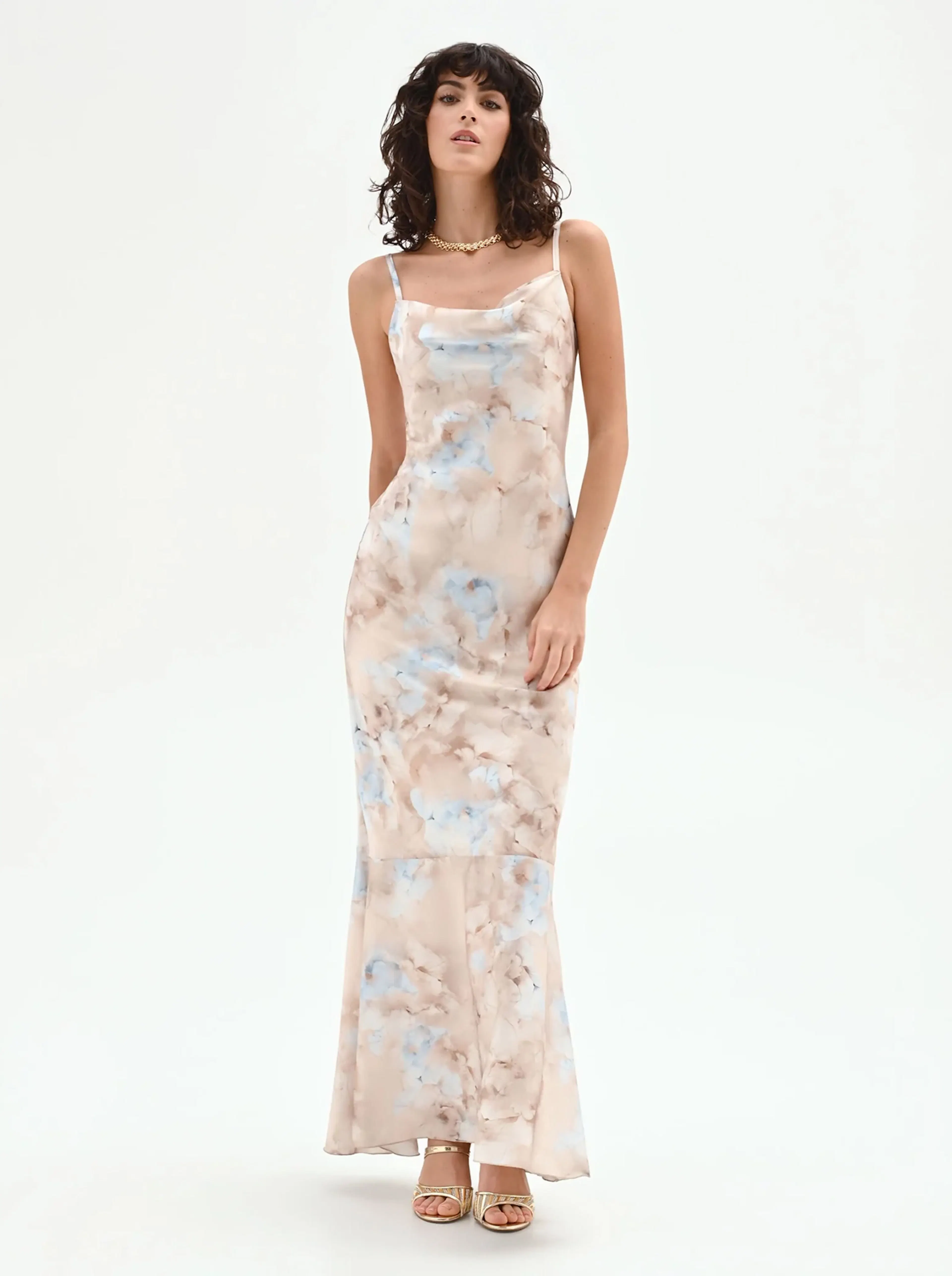 Woman in a flowy, pastel pink and blue patterned dress poses against a white background. She exudes confidence with a relaxed yet elegant stance.