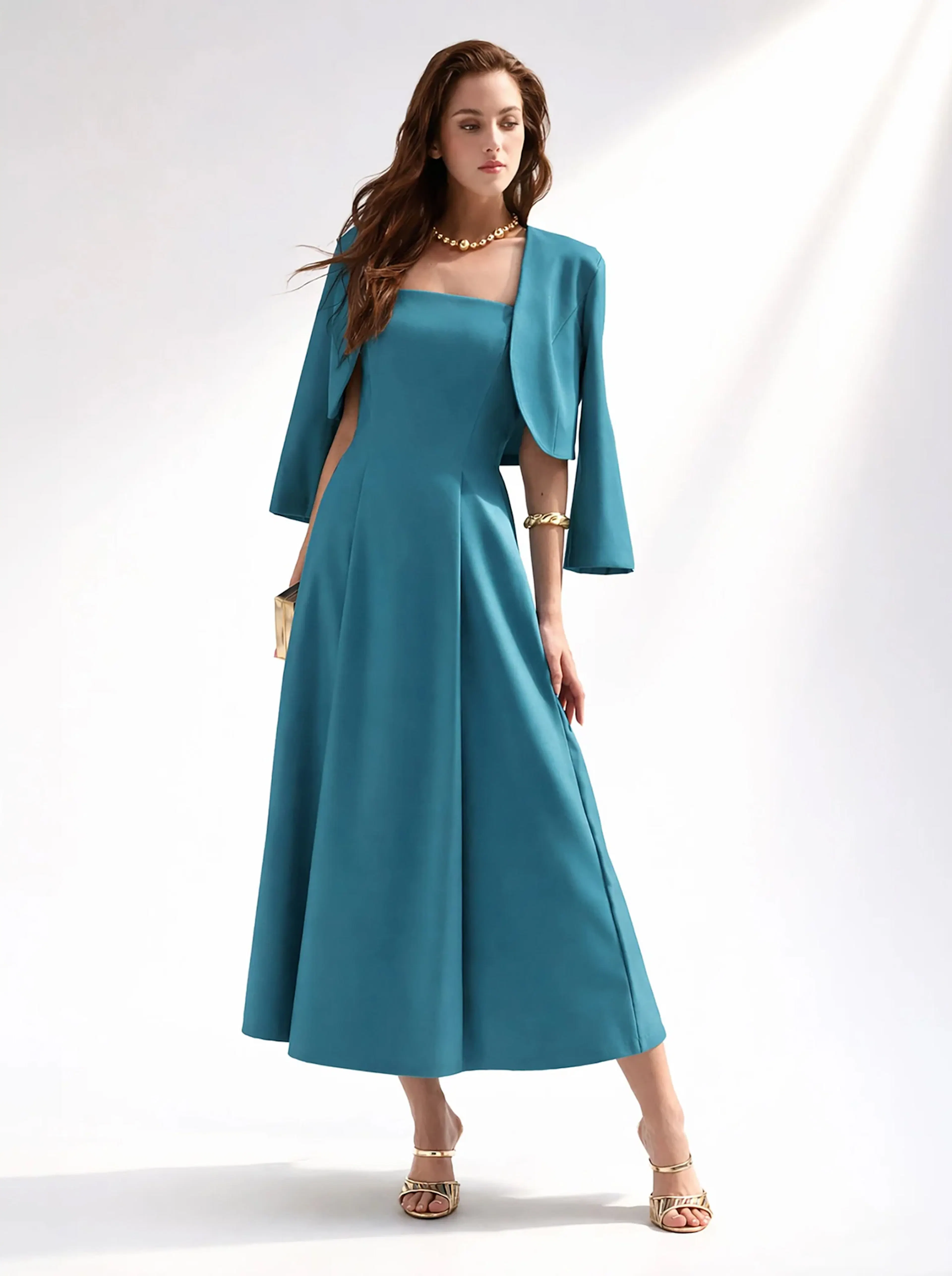 Elegant woman in a teal, floor-length gown with a matching jacket. She accessorizes with gold jewelry and sandals, exuding sophistication and grace.