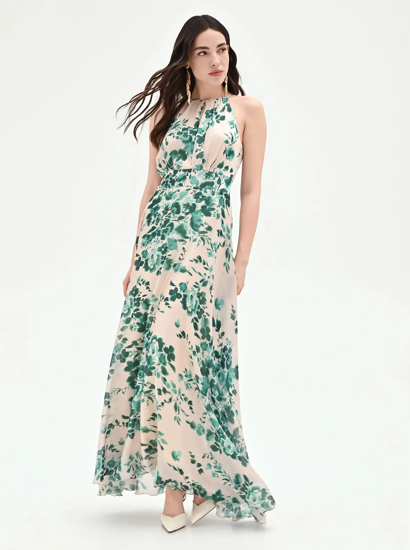 Woman in a flowing halter-neck gown with green floral patterns, standing on a white background. Her hair is loose, conveying elegance and grace.