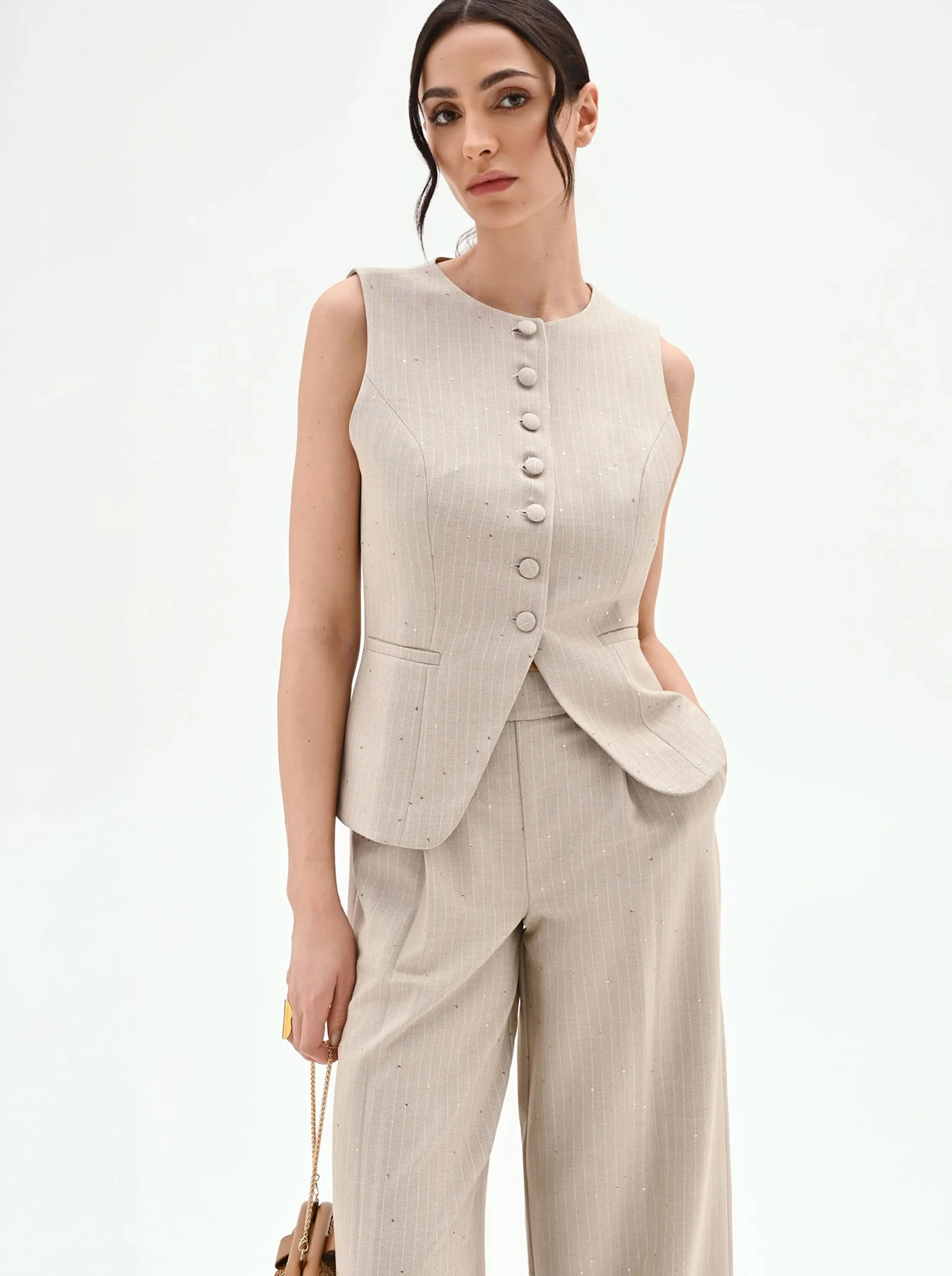 A woman poses in a sophisticated beige pantsuit with button detail, exuding elegance and confidence. Her hair is styled in loose waves, adding a chic touch.
