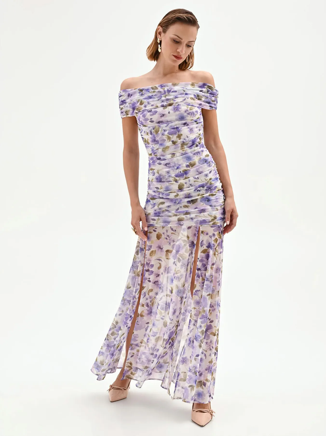 Woman in an off-shoulder, floral-print gown with purple and beige hues stands gracefully on a white background, exuding elegance and style.