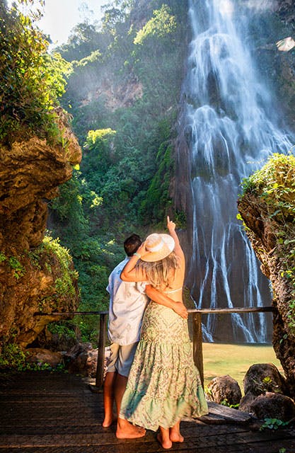 Casal contemplando cachoeira altíssima formada por águas cristalinas