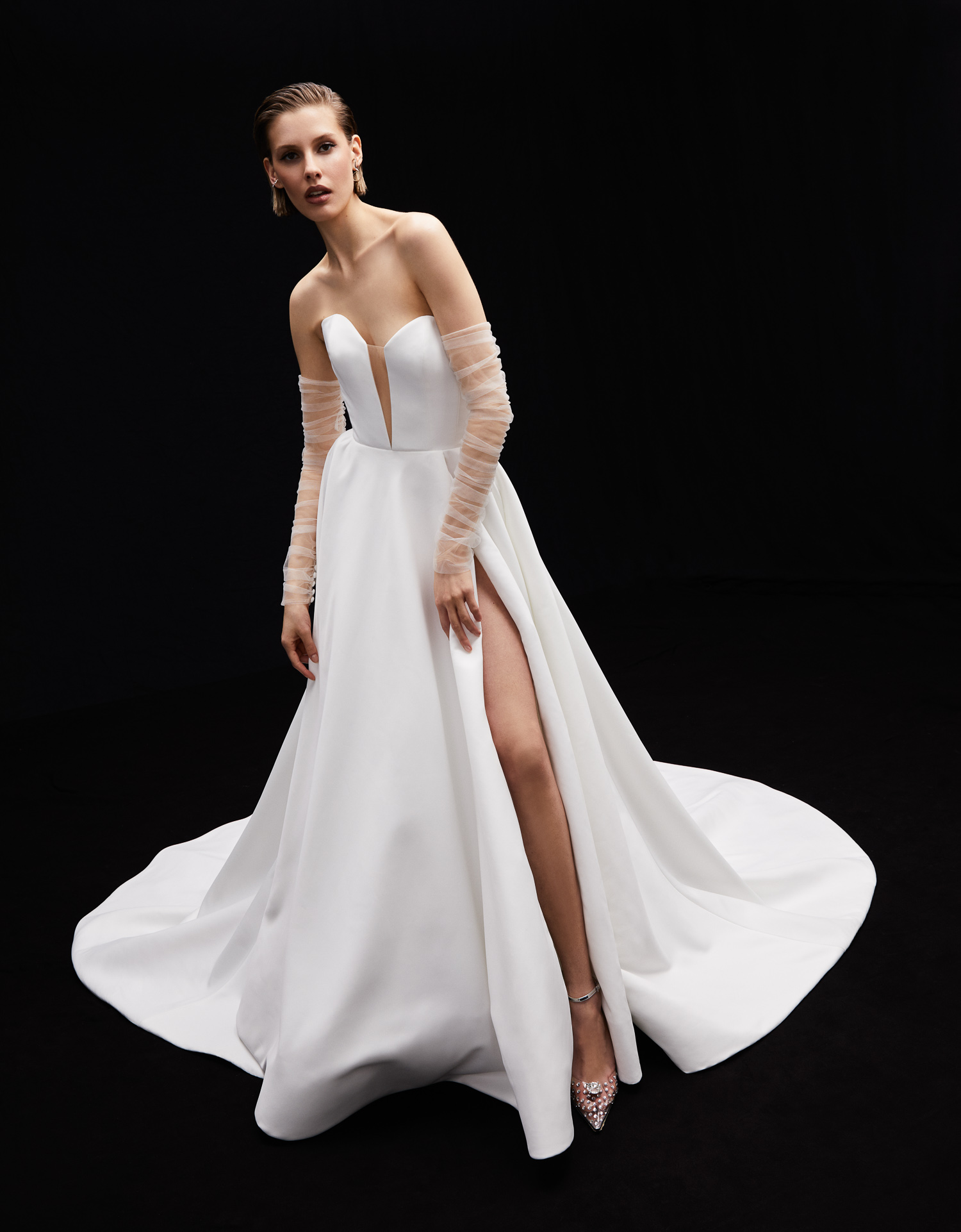 Stella matte satin ball gown with deep sweetheart neckline, front slit, exposed boning back detail, and ruched tulle sleeve, shown from the front.