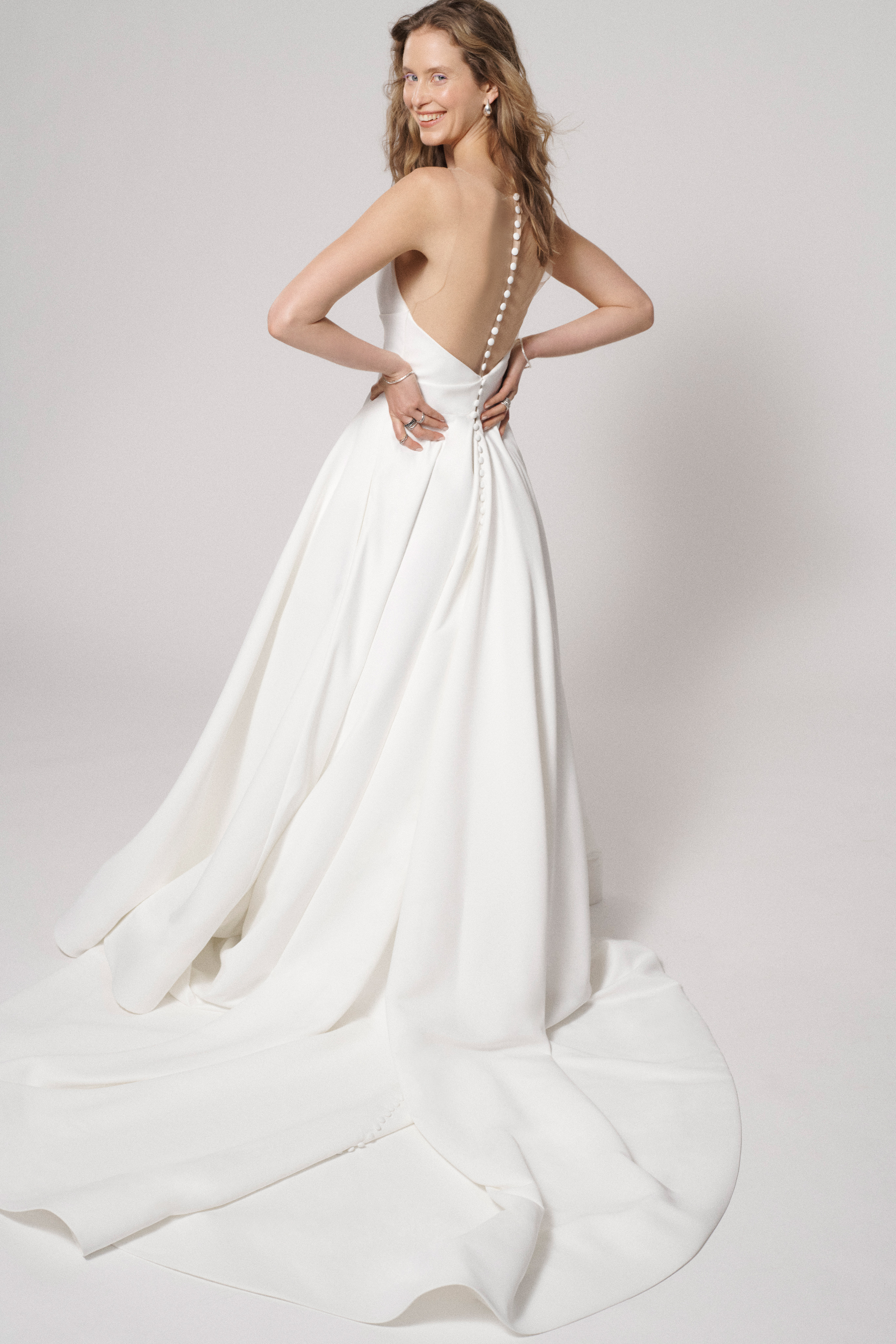 Ali ivory ball gown with draped empire waist and back button detail, shown from the side.