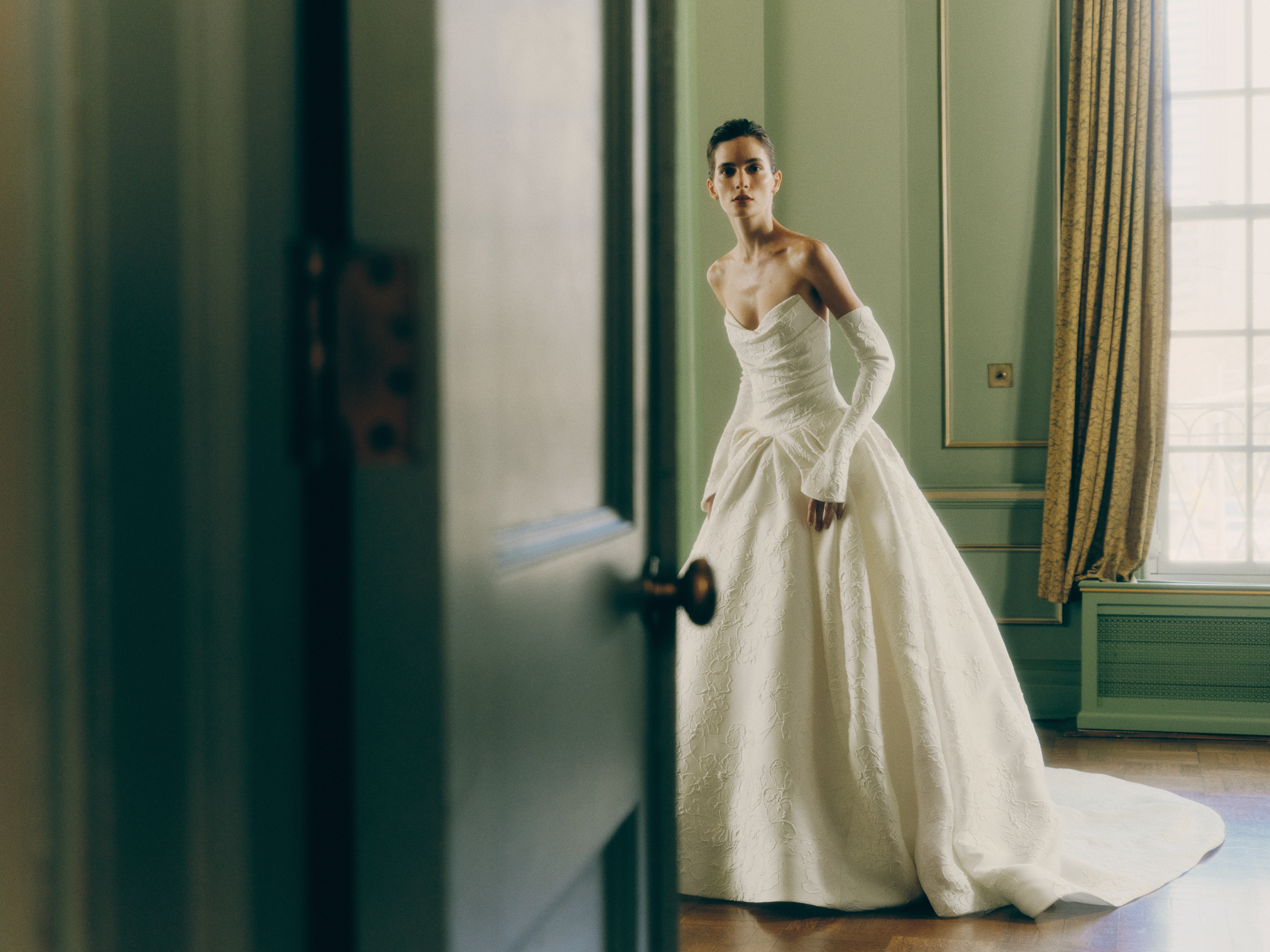 Bride wearing the Yves grand ballgown, showing the voluminous pleated skirt, opera cuffs, and pearl buttons.