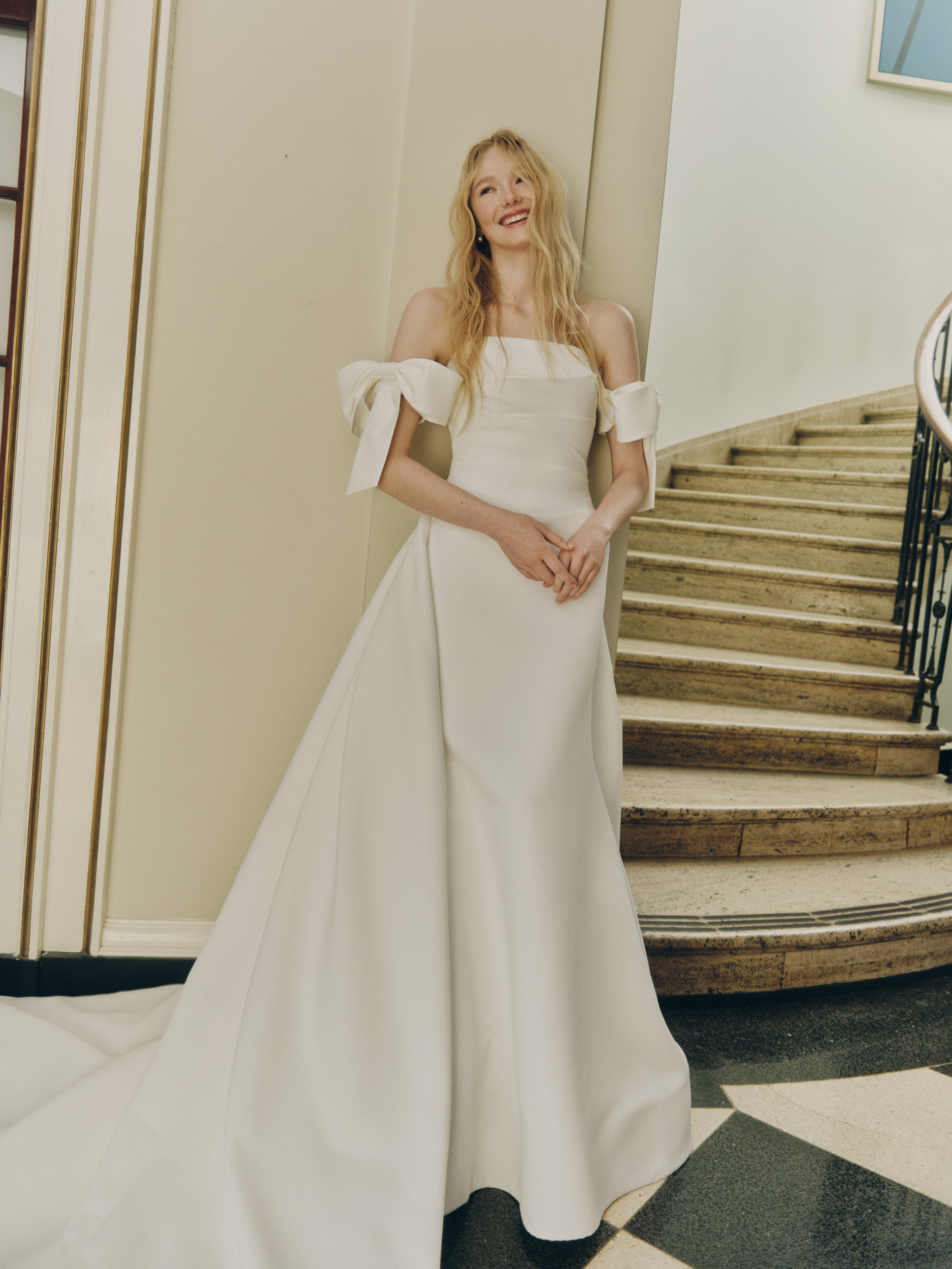 Full-length view of the Oli strapless gown with draped basque waist, pleated overskirt, and detachable bow sleeves.
