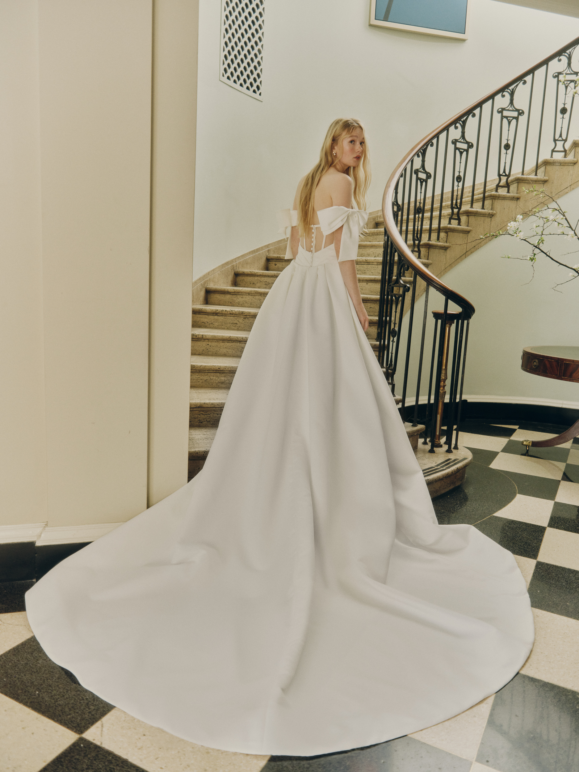 Back view of the Oli gown, showing the sheer back, exposed boning, full overskirt, and bow sleeve detail.