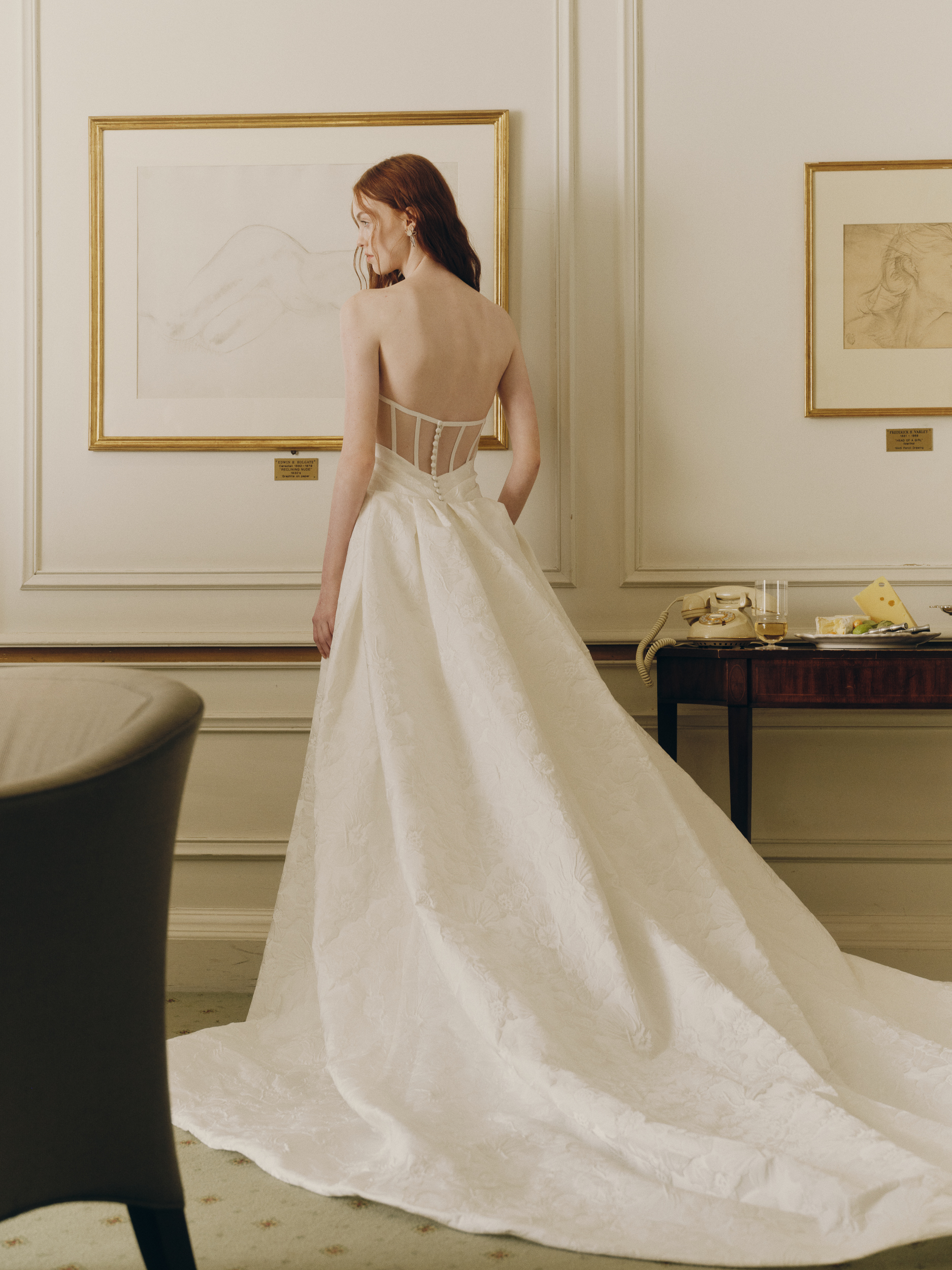 Back view of the Prie gown, showing the sheer back, exposed boning, buttons, and voluminous pleated overskirt.