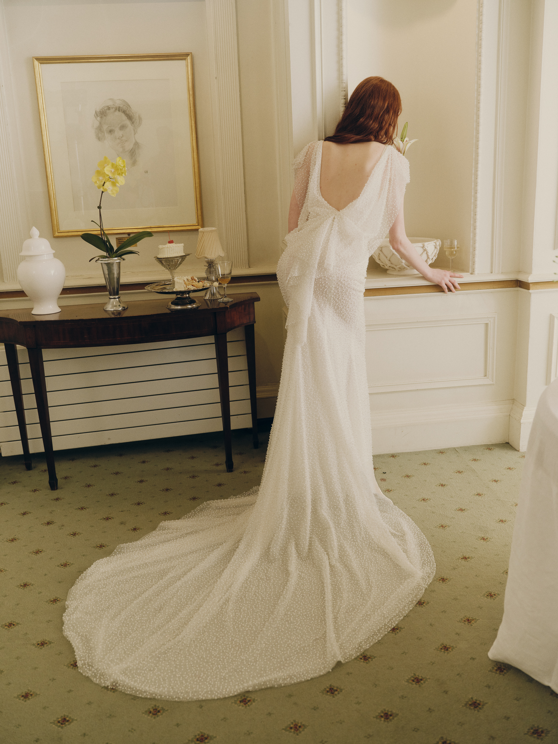 Side view of the Shia gown, showing the flutter sleeve, pearl-beaded sheath silhouette, and train.